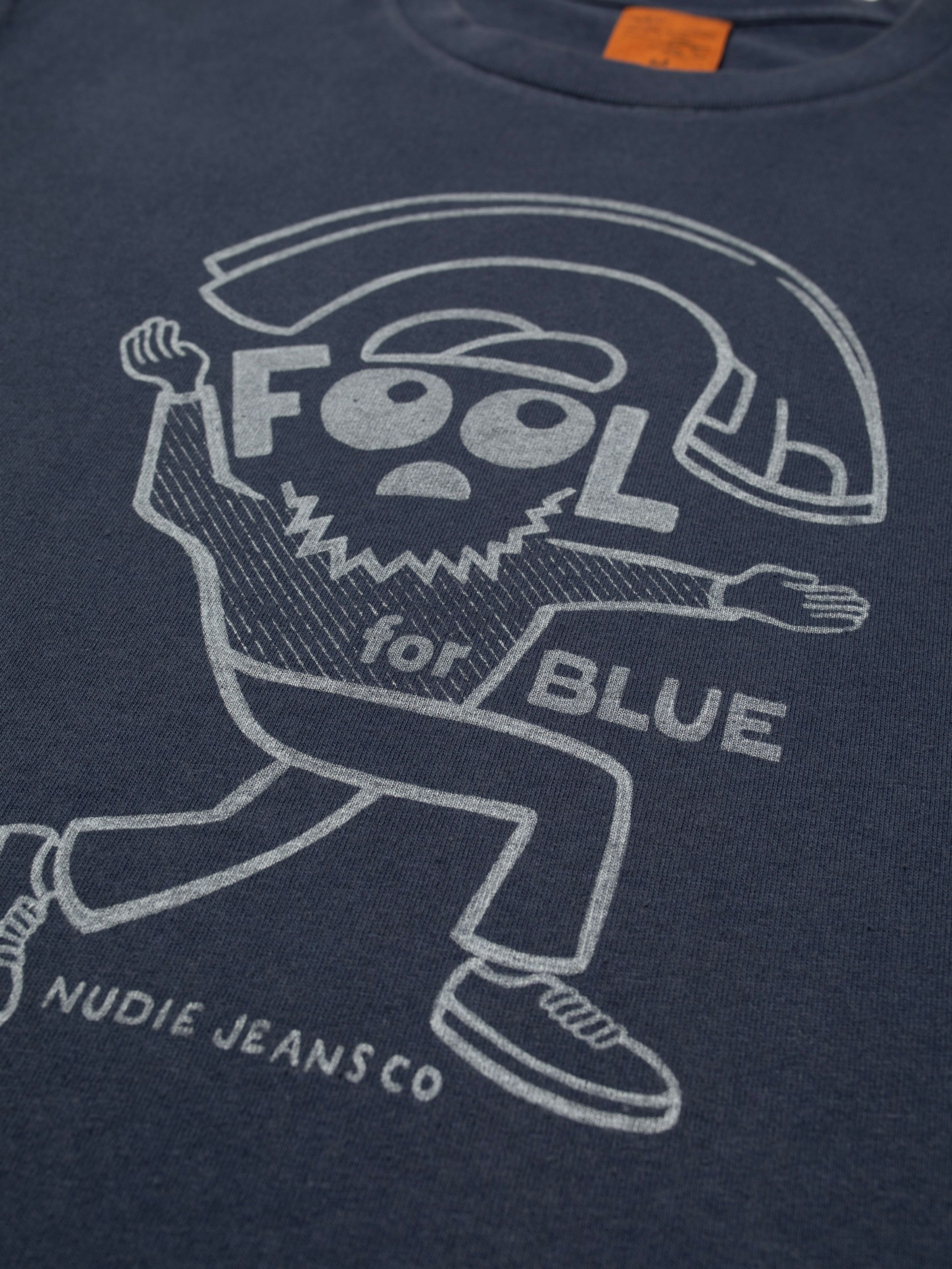 Nudie Jeans Roy T-Shirt Jeanjuggler in Dunkelblau, Nahaufnahme des „Fool for Blue“-Grafikdrucks auf Bio-Baumwolle.