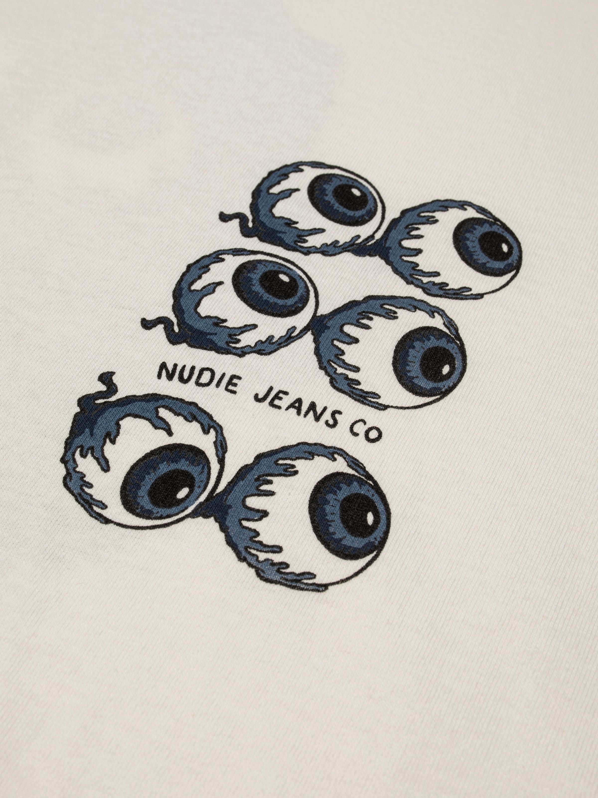 Nudie Jeans Roy T-Shirt Wall Crack in Chalk White, Nahaufnahme der Augapfel-Grafik und Logo-Print auf Bio-Baumwolle.