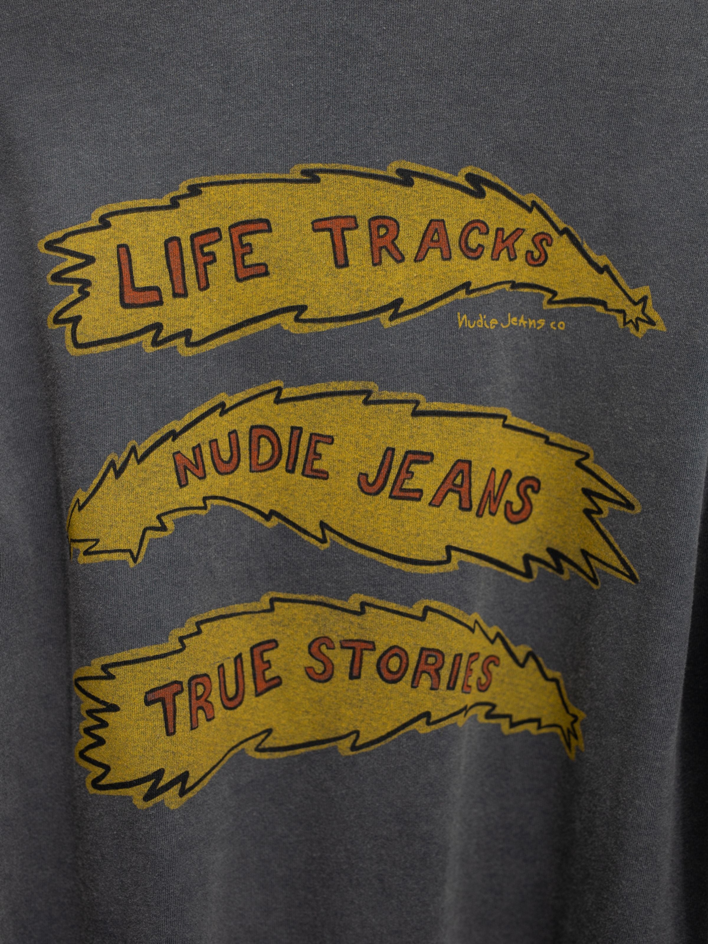 Close-up of the yellow Life Tracks graphic on the Nudie Jeans Rudi long-sleeve t-shirt in Antracite organic cotton.