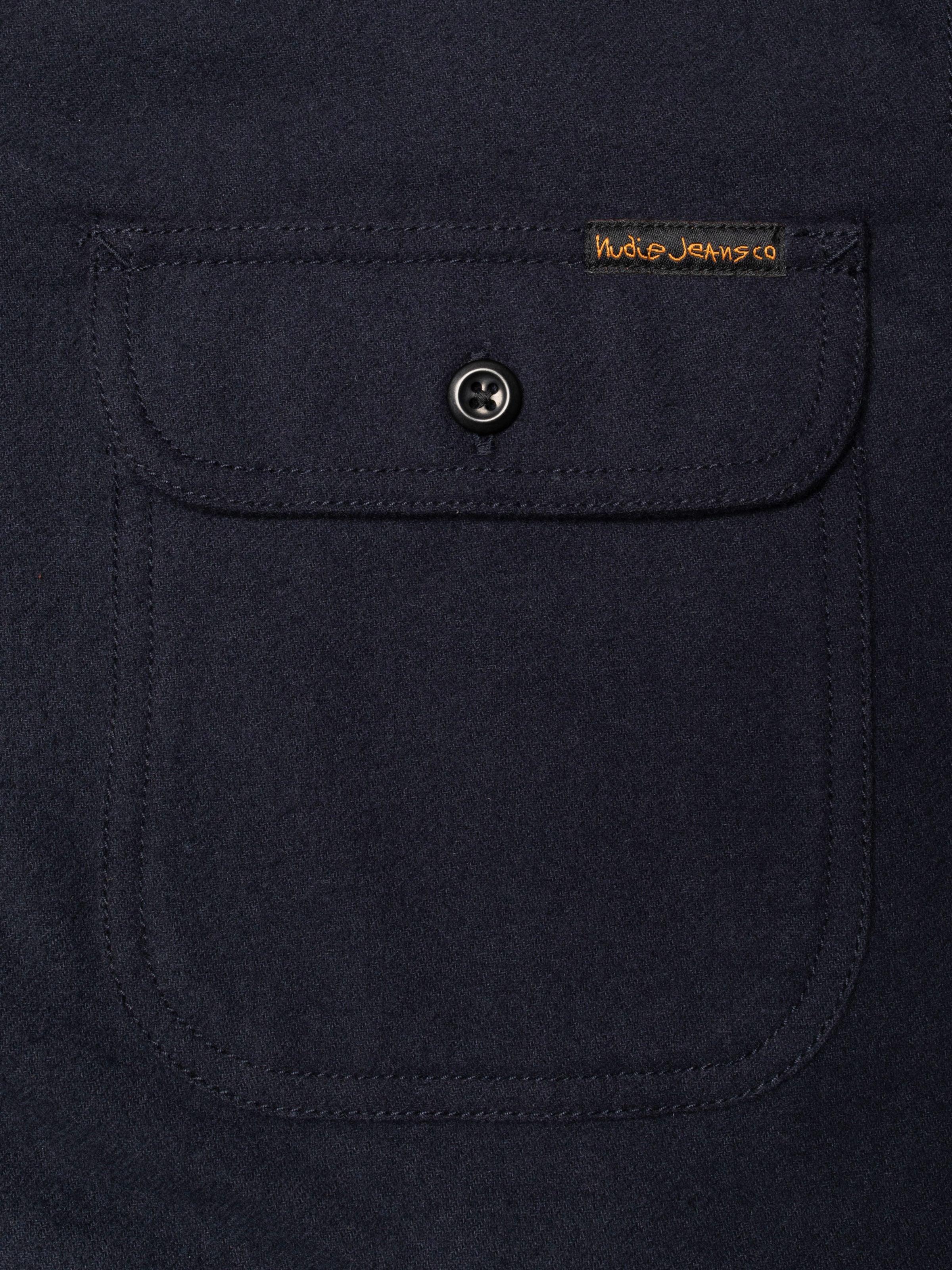 Nudie Jeans Glenn Padded Shirt Flannel in Blueberry, Nahaufnahme von Brusttasche und Label aus Flanell aus Bio-Baumwolle.