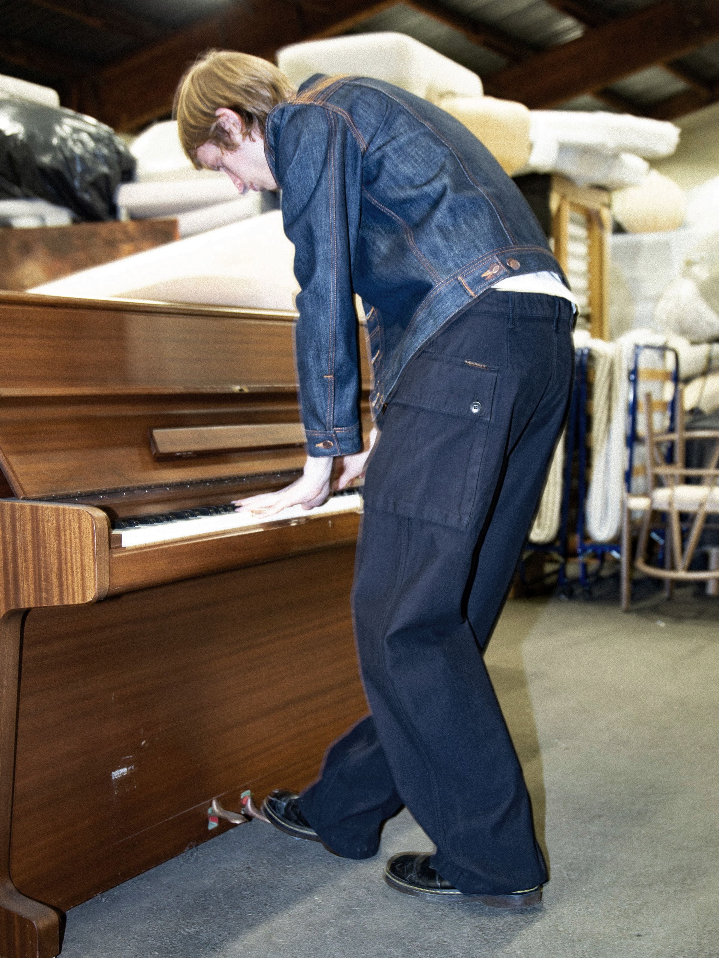 Nudie Jeans Loud Larry Pants Back Sateen, indigo organic cotton cargo pants shown on a model playing a piano.