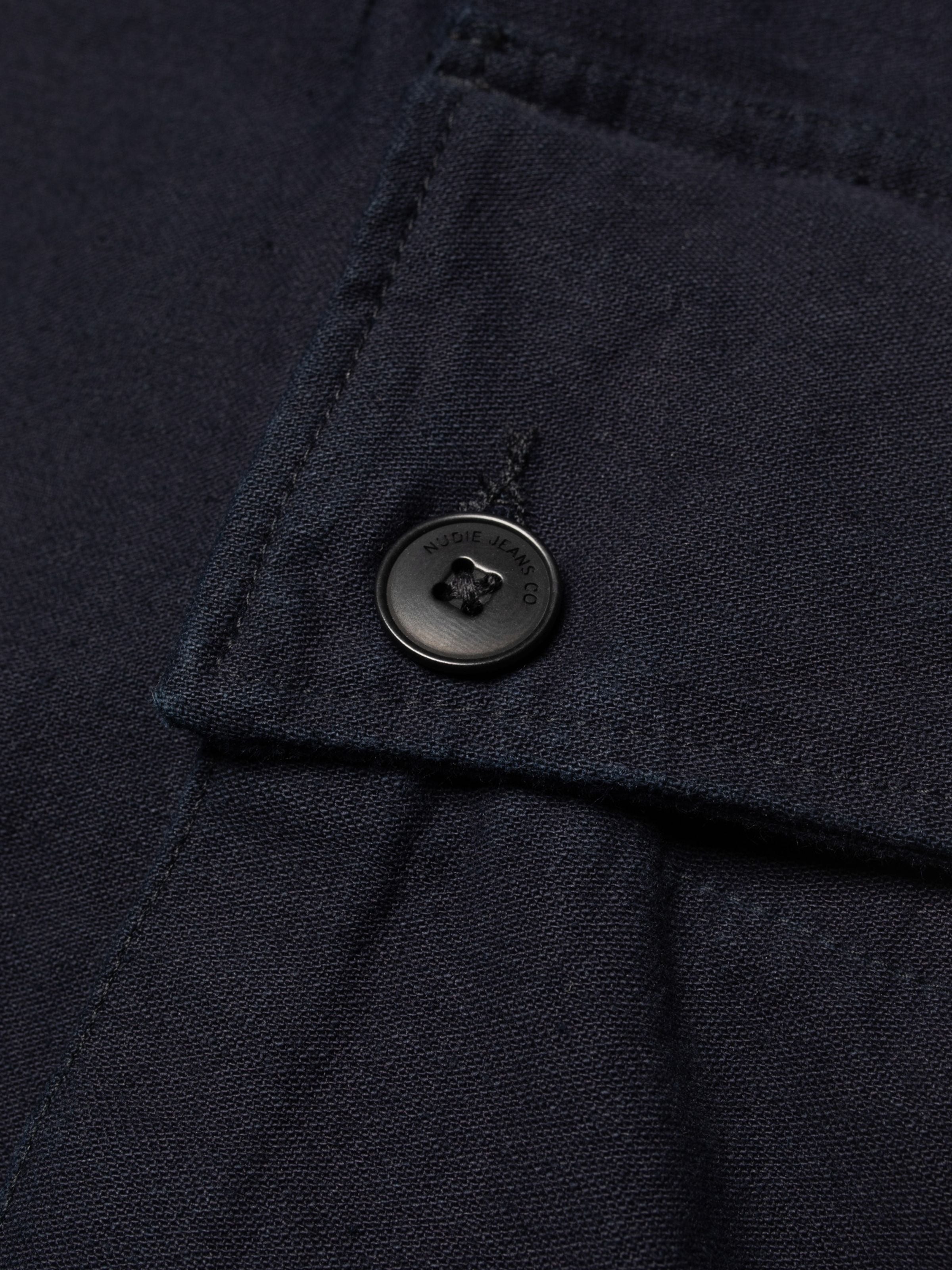 Nudie Jeans Loud Larry Pants Back Sateen, close-up of the branded button on the indigo organic cotton fabric.