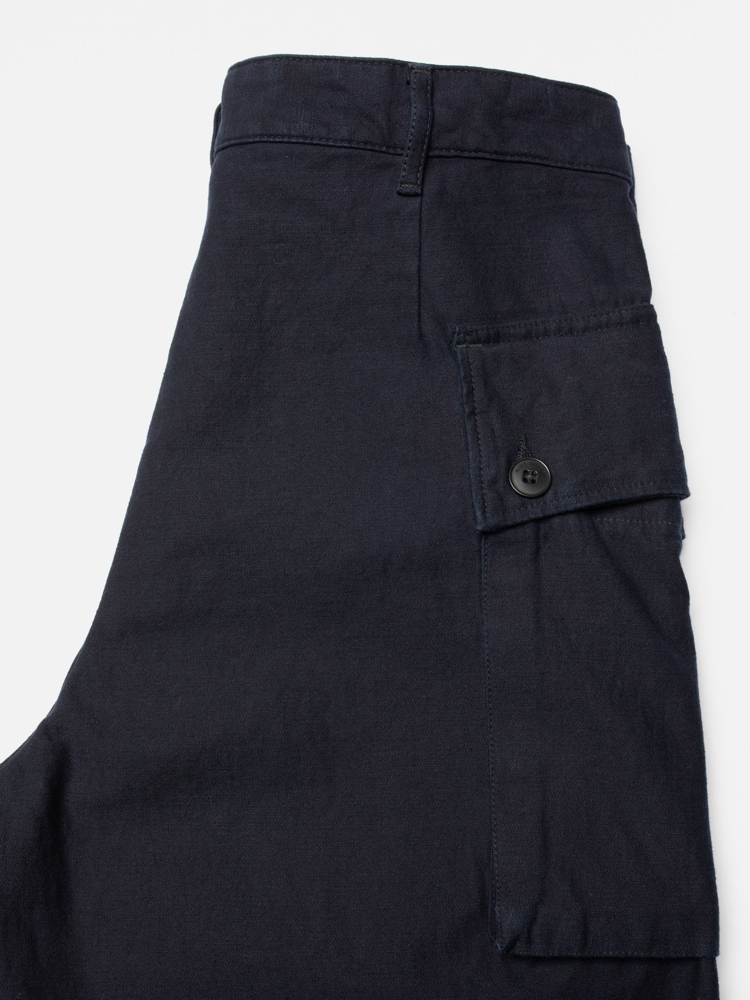 Nudie Jeans Loud Larry Pants Back Sateen, close-up of the large cargo pocket on dark indigo organic cotton fabric.