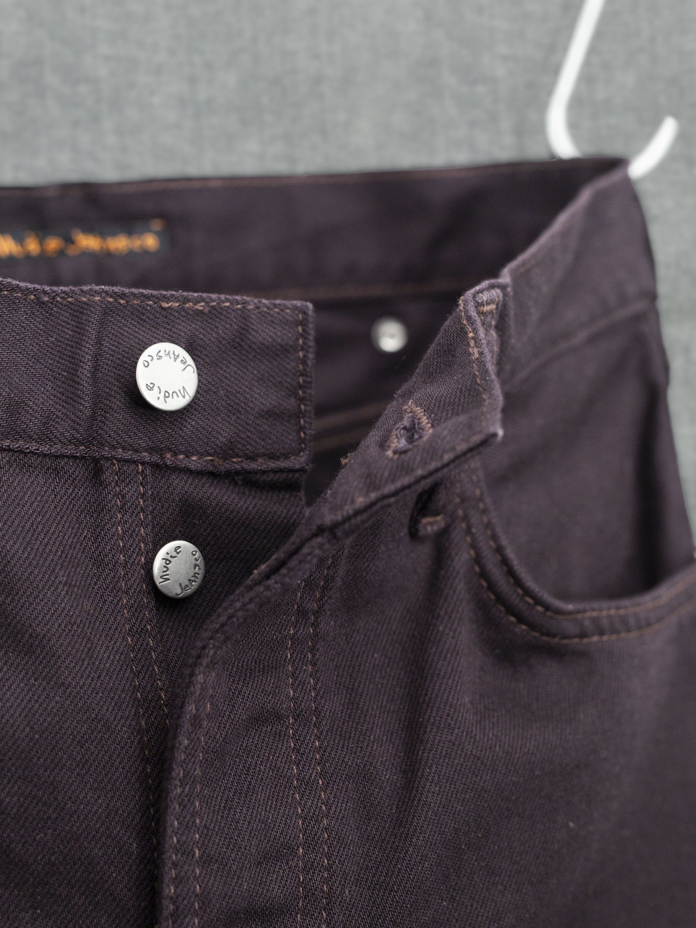 Nudie Jeans Rad Rufus Everbrown, Detailaufnahme der Knopfleiste und silbernen Metalldetails auf tiefbraunem Rigid Denim.