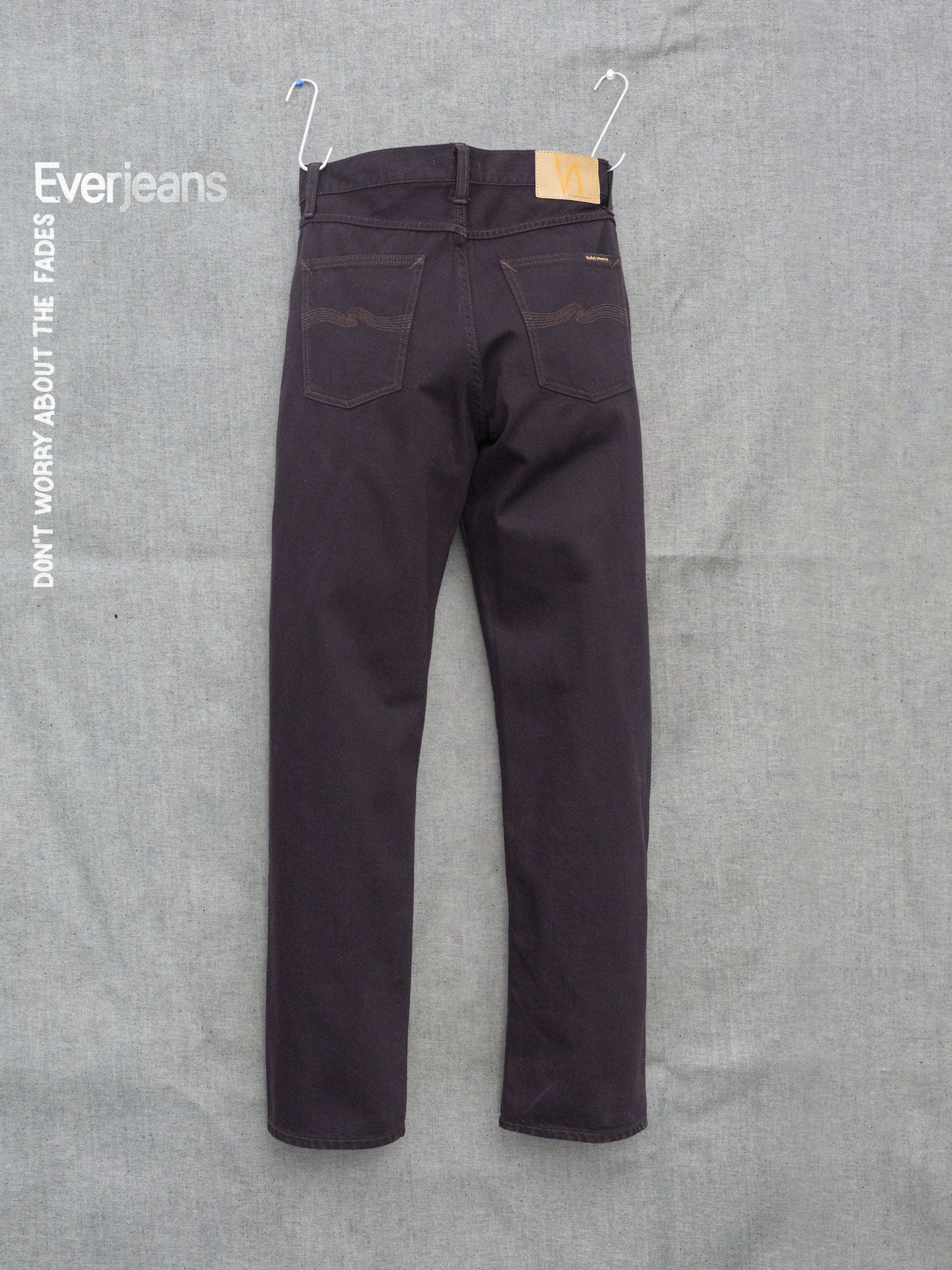 Nudie Jeans Rad Rufus Everbrown, Herrenjeans in Braun von hinten vor strukturiertem Hintergrund.