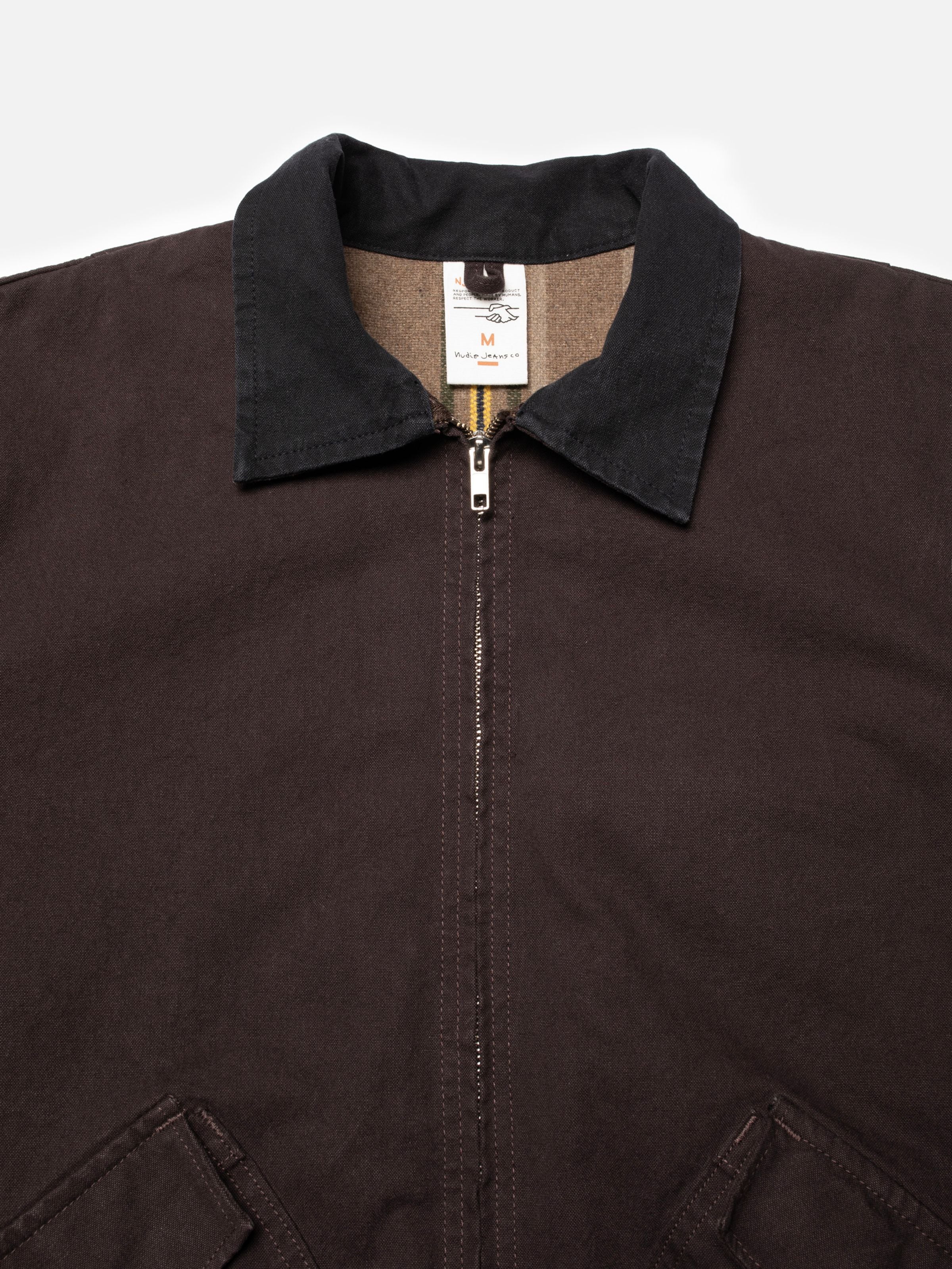 Nudie Jeans Blake Zip Jacket Duck Canvas in Dunkelbraun aus Bio-Baumwolle mit schwarzem Kragen und silbernem Reißverschluss.