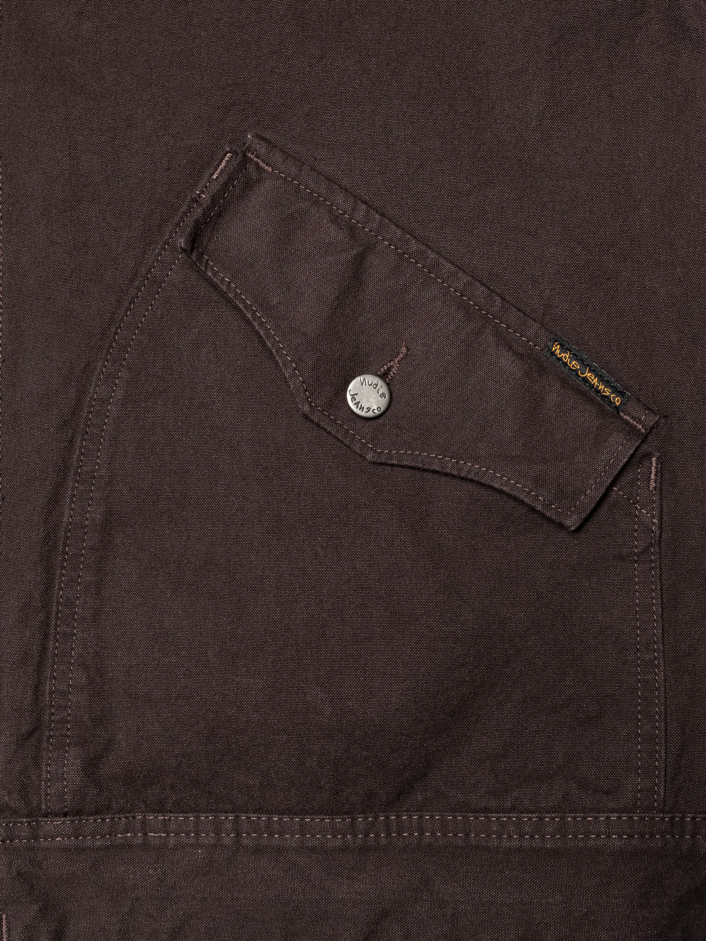 Nudie Jeans Blake Zip Jacket Duck Canvas in Dunkelbraun, Nahaufnahme der geschwungenen Tasche aus Bio-Baumwolle.