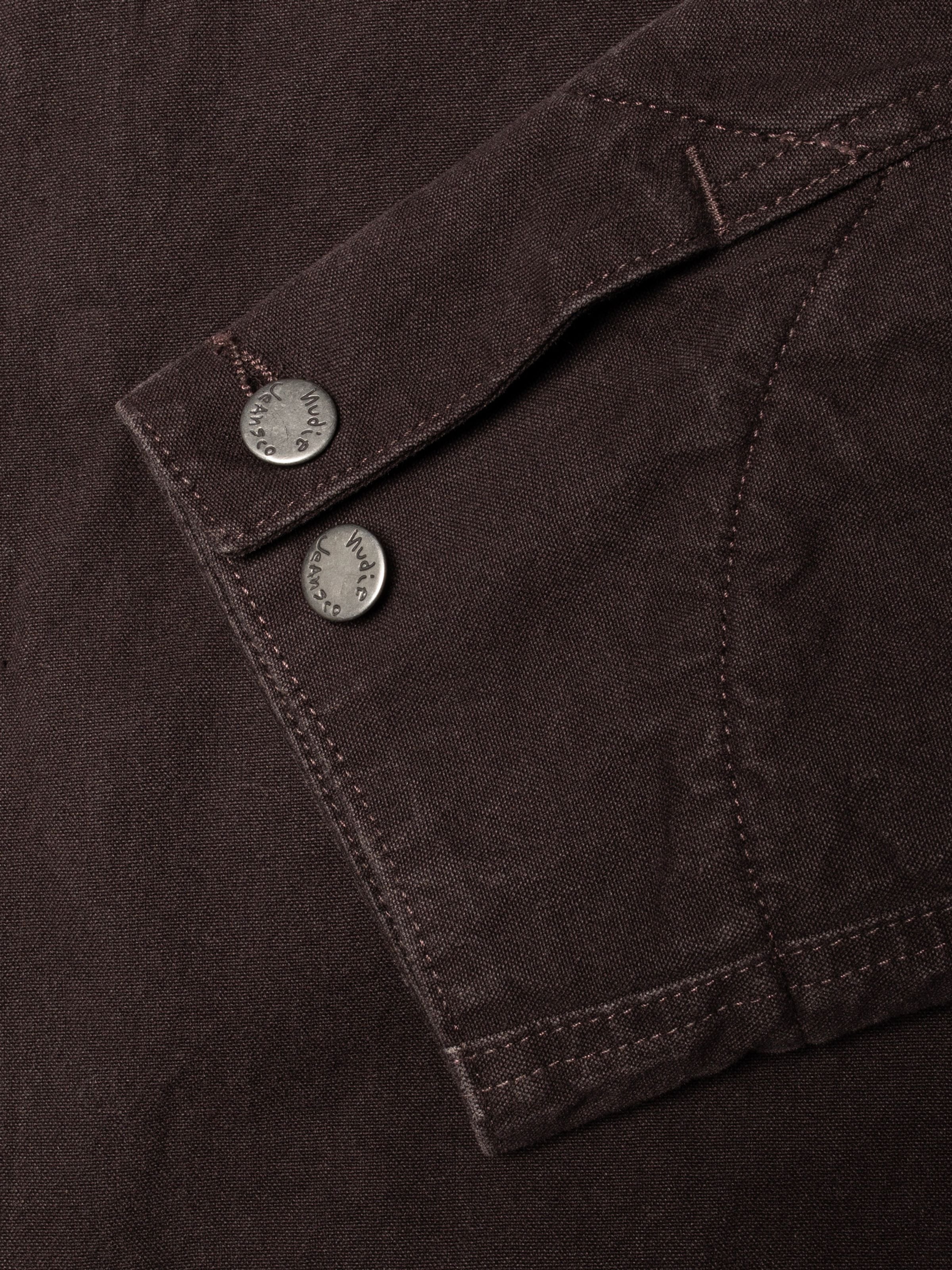 Nudie Jeans Blake Zip Jacket in Dunkelbraun, Nahaufnahme von antik-silbernen Logo-Knöpfen und Bio-Baumwolle Duck Canvas.