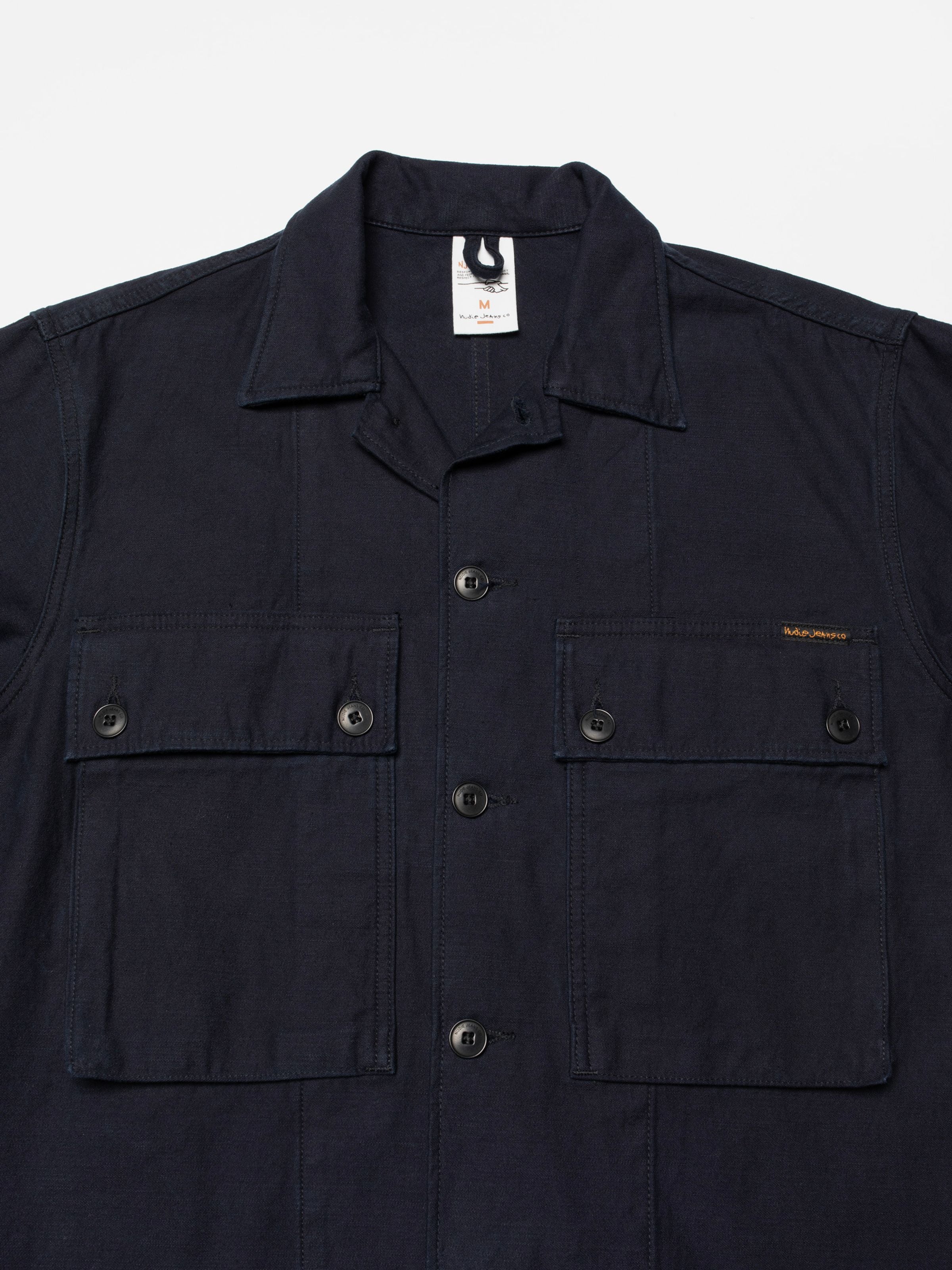 Nudie Jeans Nino Shirt Back Sateen Indigo, Nahaufnahme der Vorderseite mit Brustpattentaschen und Stoff aus Bio-Baumwolle.