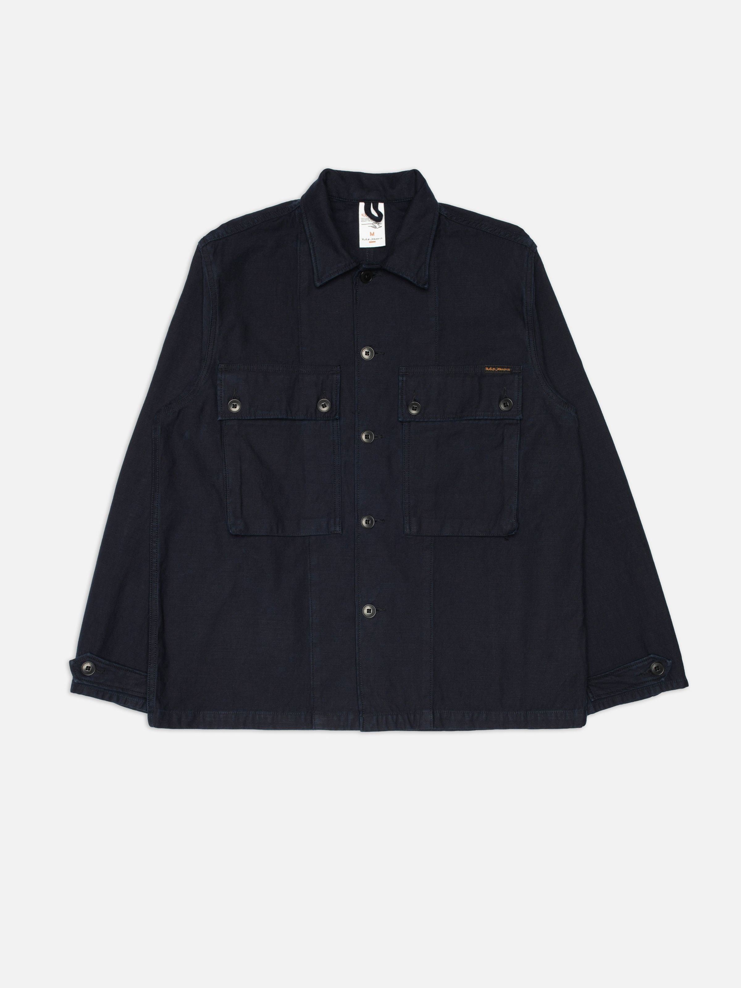 Nudie Jeans Nino Shirt Back Sateen Indigo, ein Overshirt aus Bio-Baumwolle mit Brusttaschen, flach liegend gezeigt.