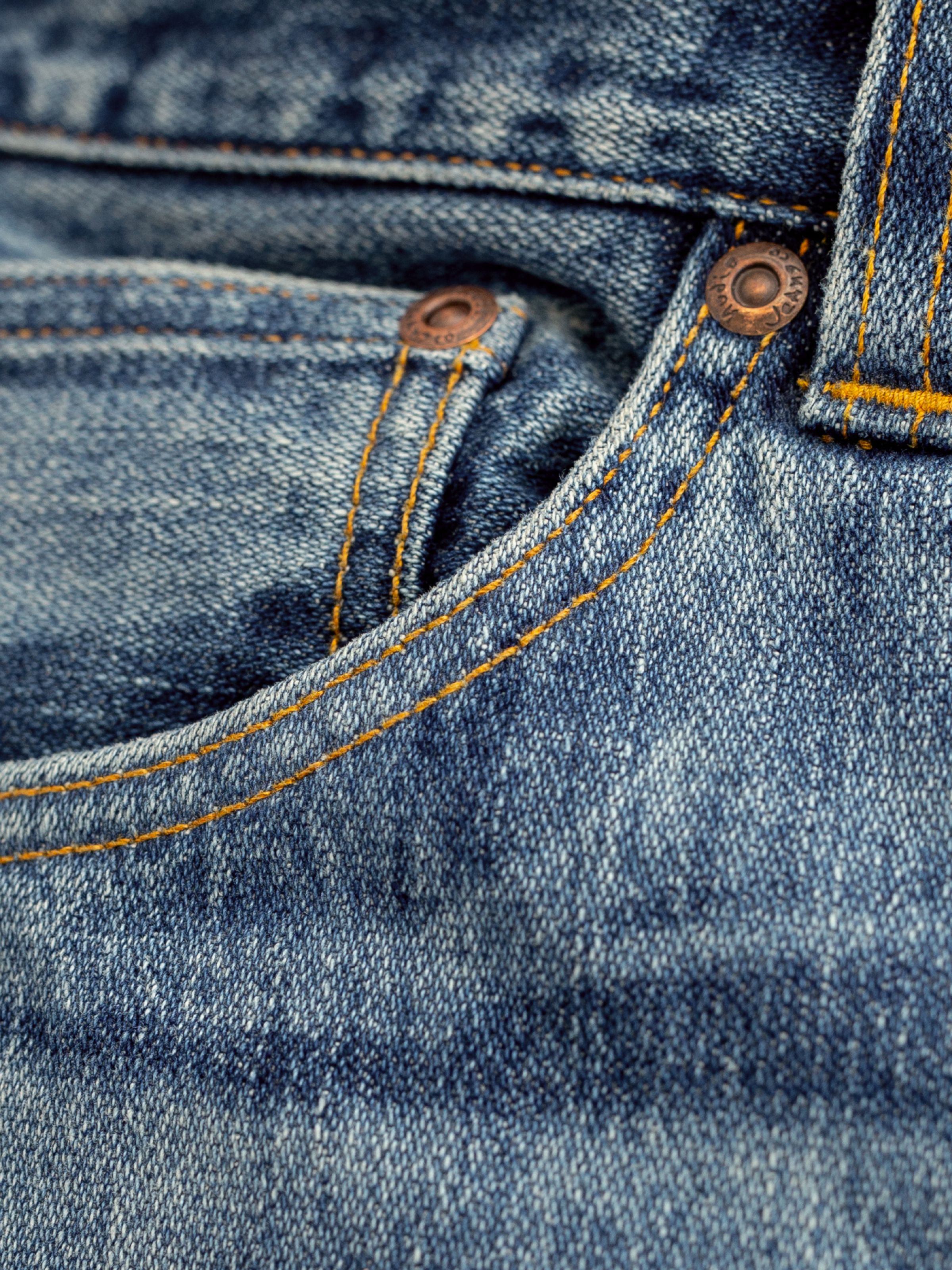 Nudie Jeans Loud Larry Muted Tracks, men's loose fit jeans, close-up of the front pocket showing the copper rivet detail.