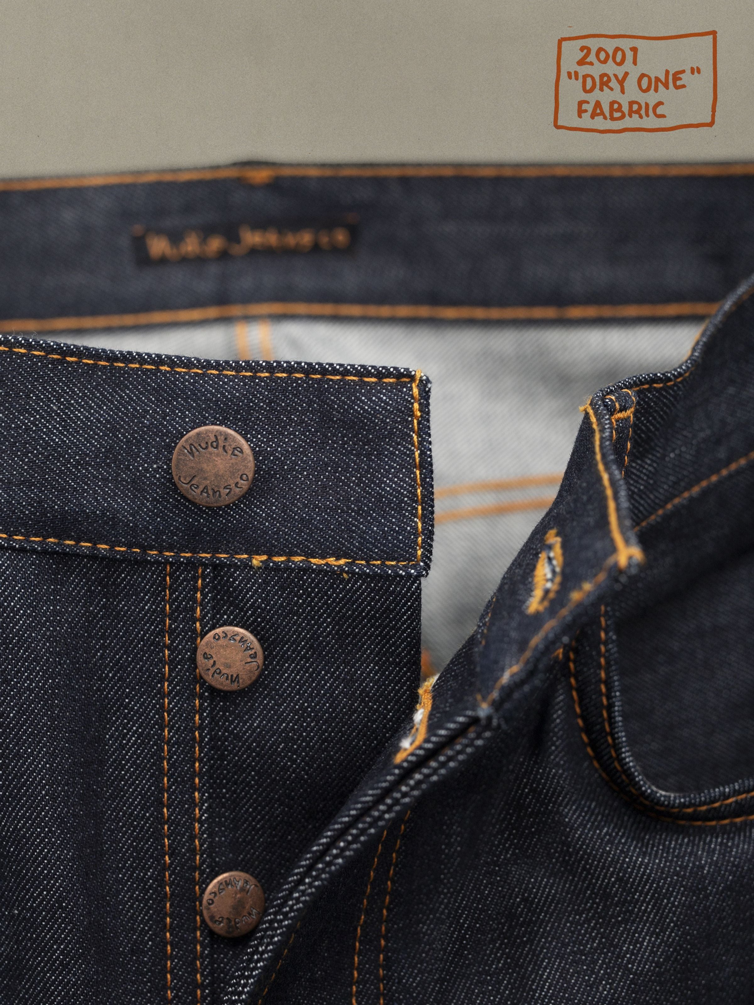 Nudie Jeans Tuff Tony Dry Ecru Waves, Nahaufnahme der Kupferknopfleiste und orangen Nähte auf Rigid Denim aus Bio-Baumwolle.