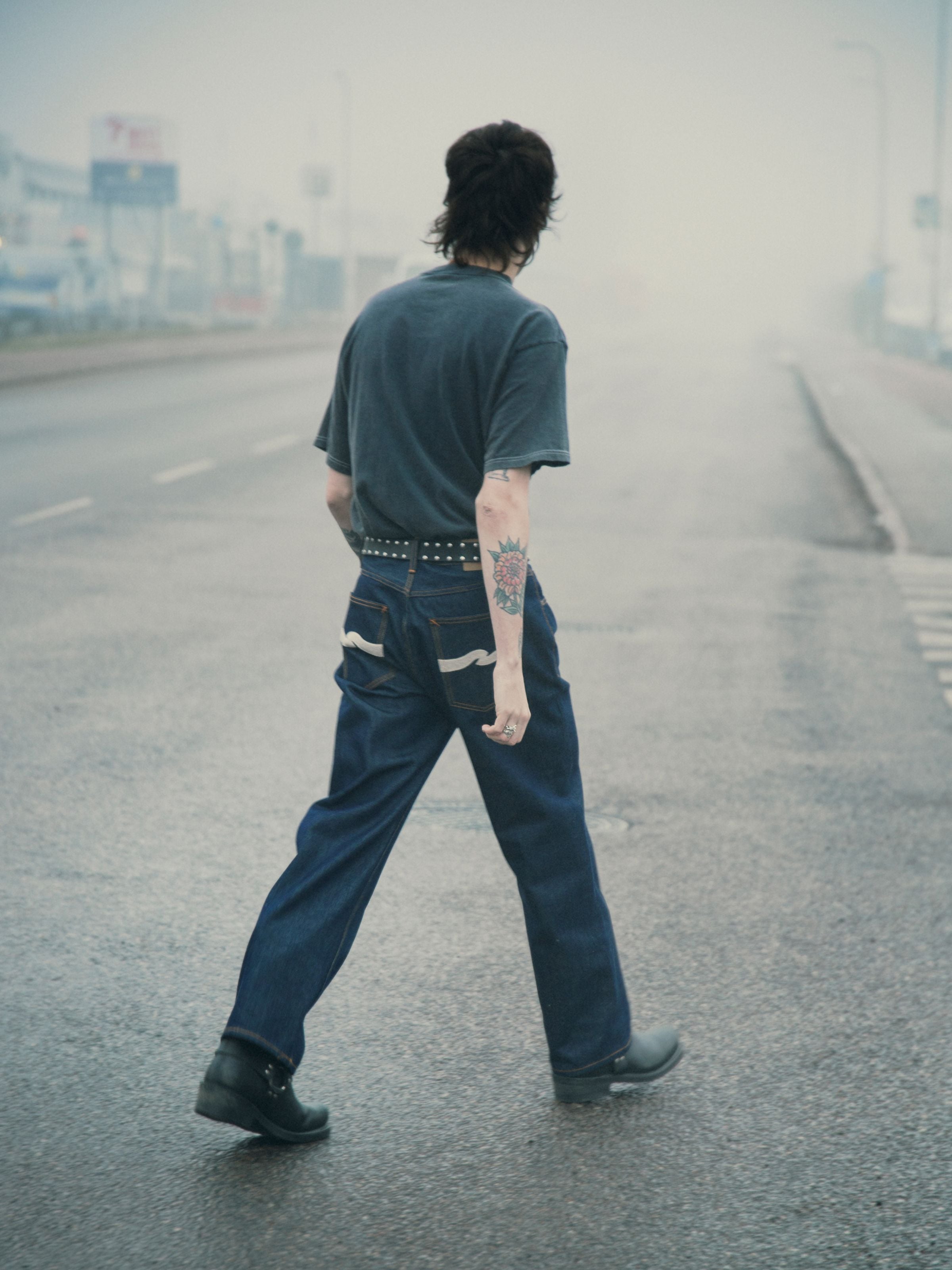 Nudie Jeans Tuff Tony Dry Ecru Waves, lockere Rigid Jeans aus Bio-Baumwolle mit Ecru-Back-Pocket-Stickerei, an einem Model.