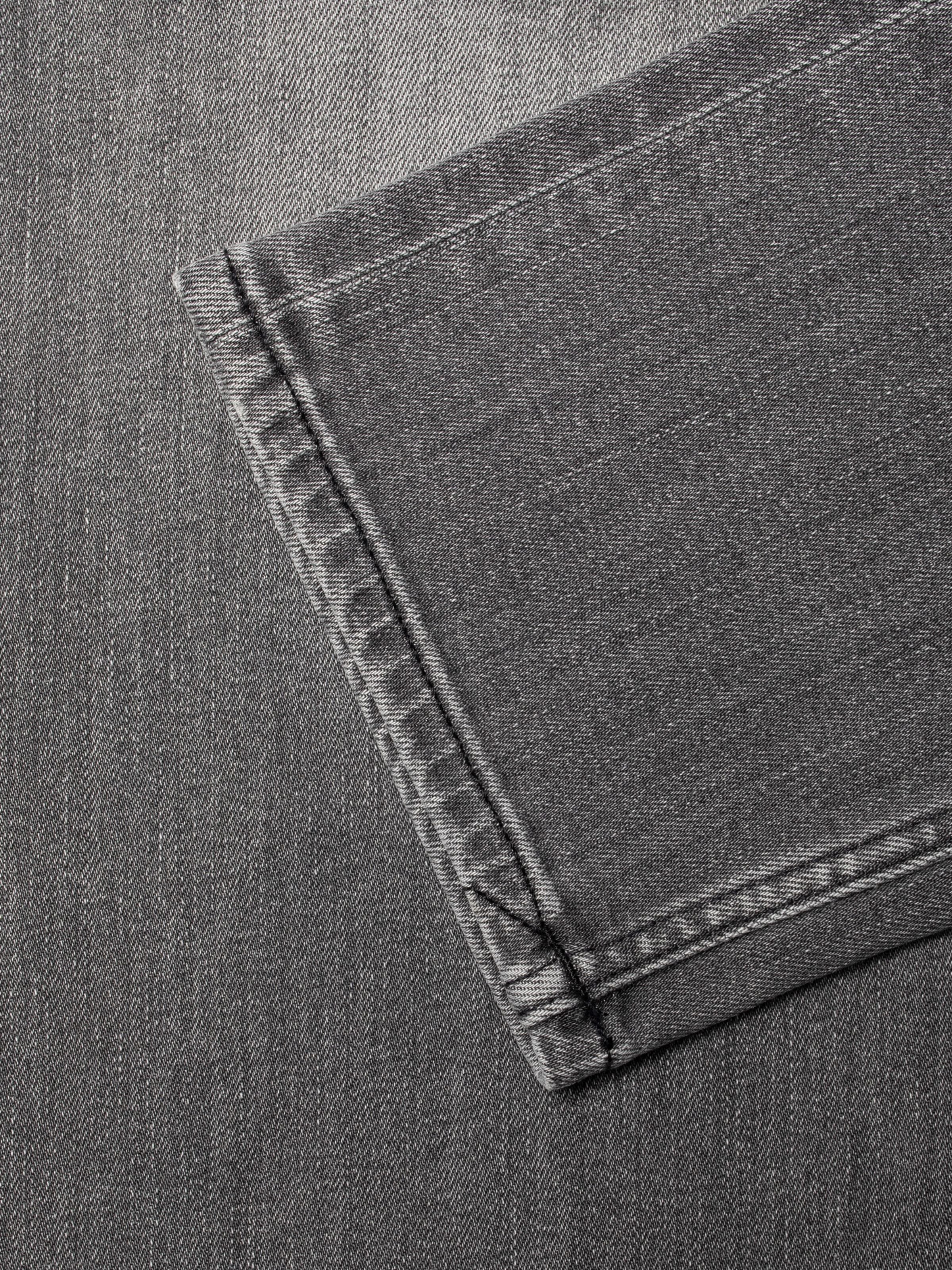 Nudie Jeans Lean Dean Grey Asphalt, close-up of the hem showing grey organic cotton denim and black thread seams.