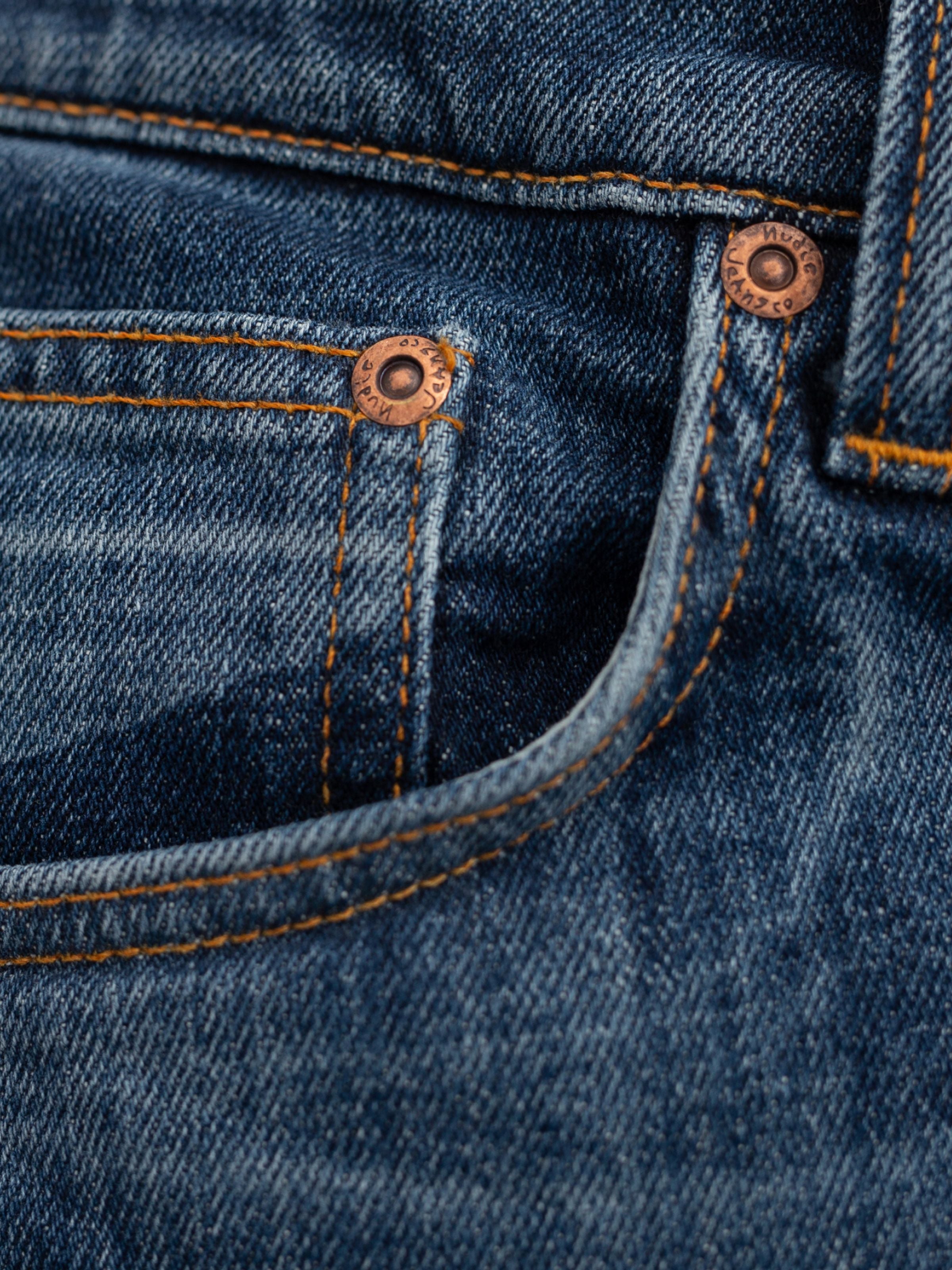 Nudie Jeans Solid Ollie Blue Echo Tracks, a close-up of blue organic cotton denim with orange stitching and copper rivets.