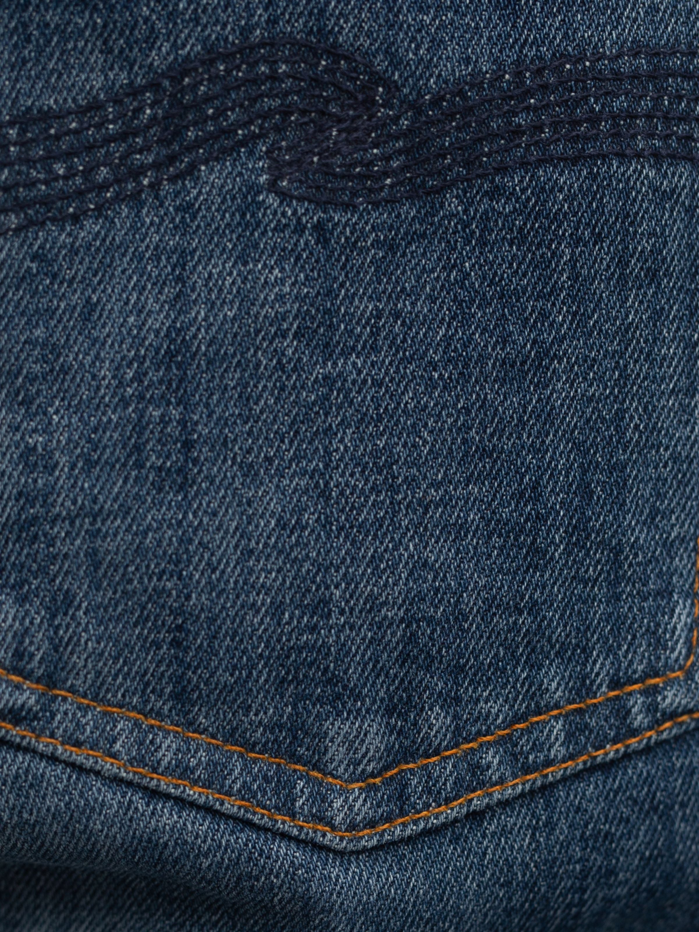 Nudie Jeans Solid Ollie Blue Echo Tracks, a close-up of blue organic cotton denim with orange stitching and navy embroidery.