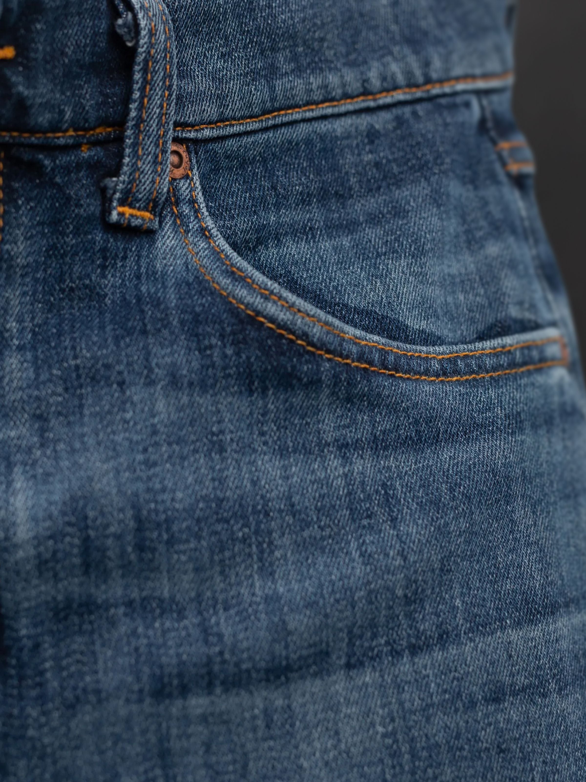 Nudie Jeans Solid Ollie Blue Echo Tracks, close-up of the front pocket and orange stitching on washed blue organic cotton.