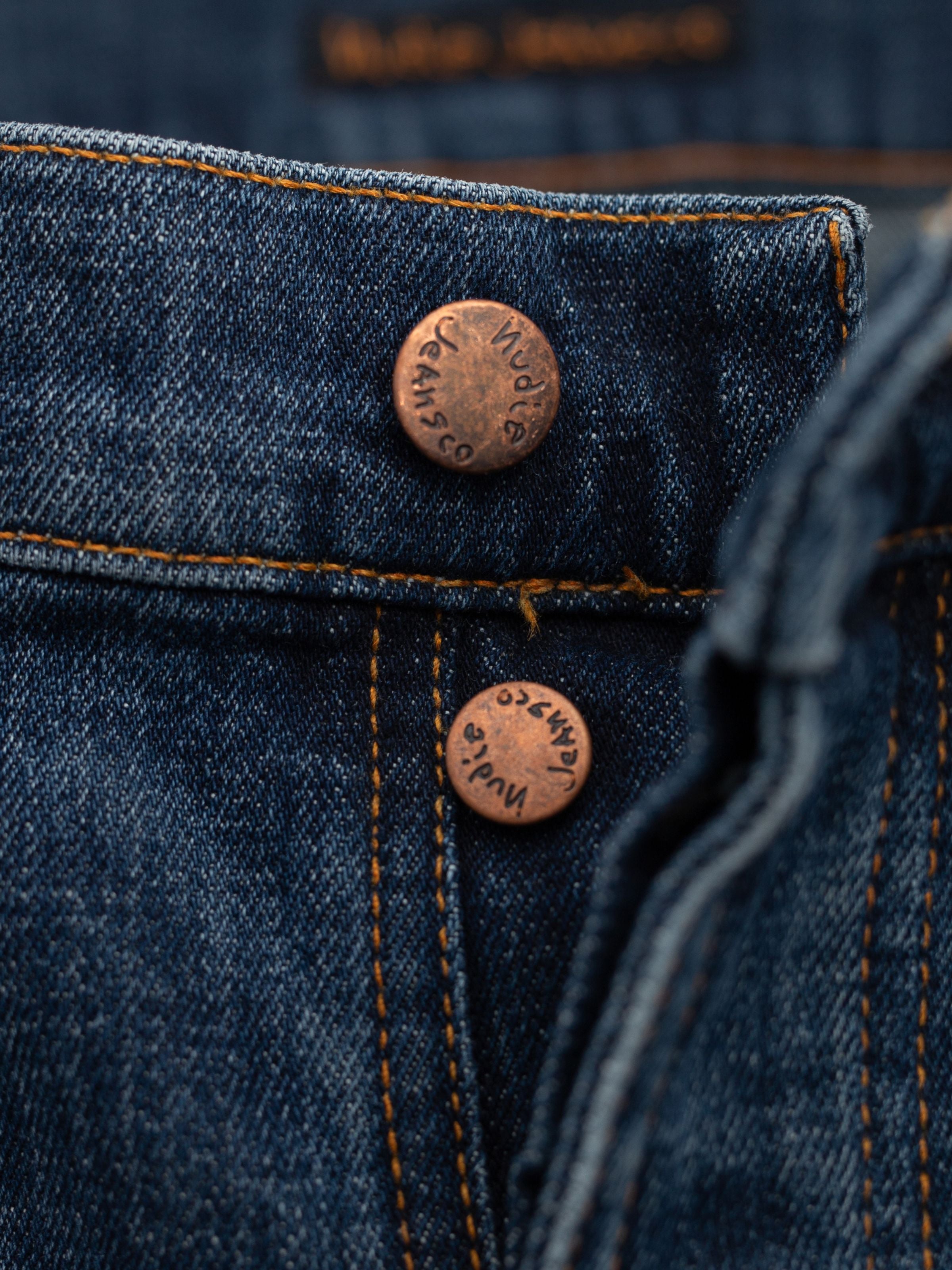 Nudie Jeans Solid Ollie Blue Echo Tracks, featuring copper buttons and orange stitching on washed blue organic cotton denim.