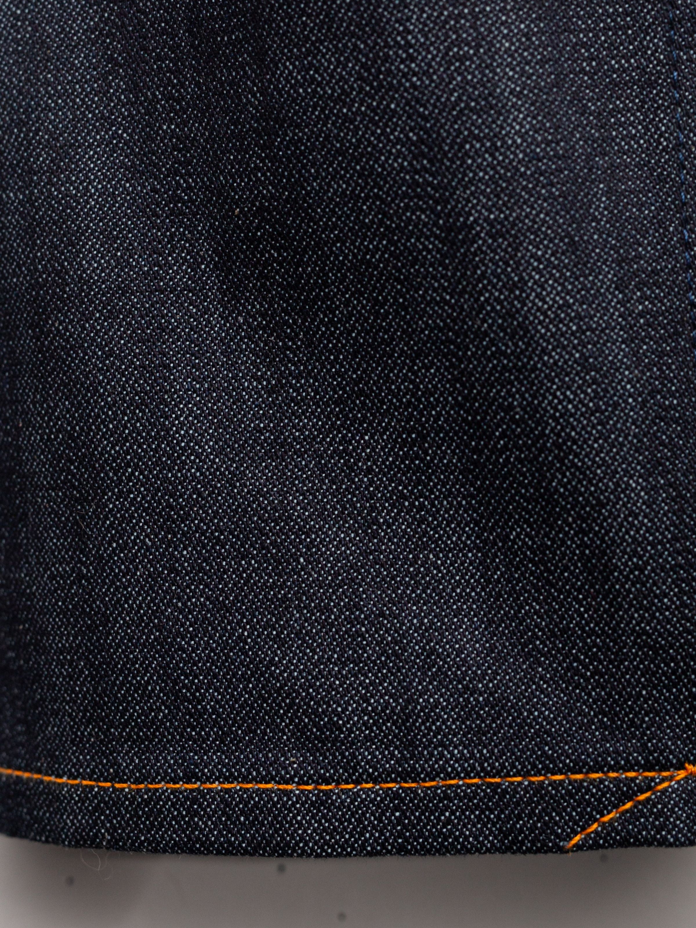 Nudie Jeans Gritty Jackson Blue Dry Two, a close-up of the dark indigo rigid organic cotton denim with orange stitching.