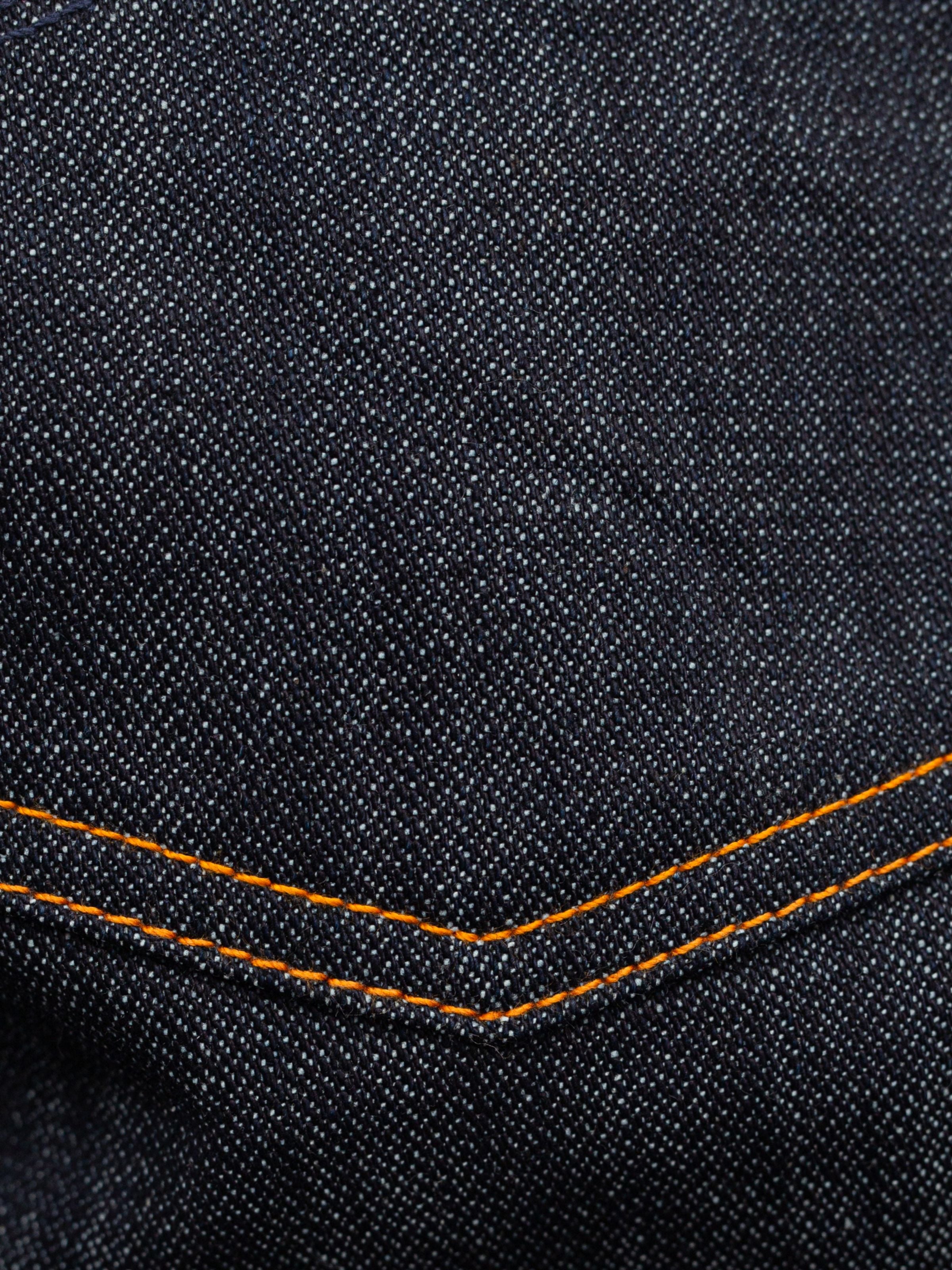 Nudie Jeans Gritty Jackson Blue Dry Two, a close-up of the rigid dark indigo organic cotton denim with orange stitching.