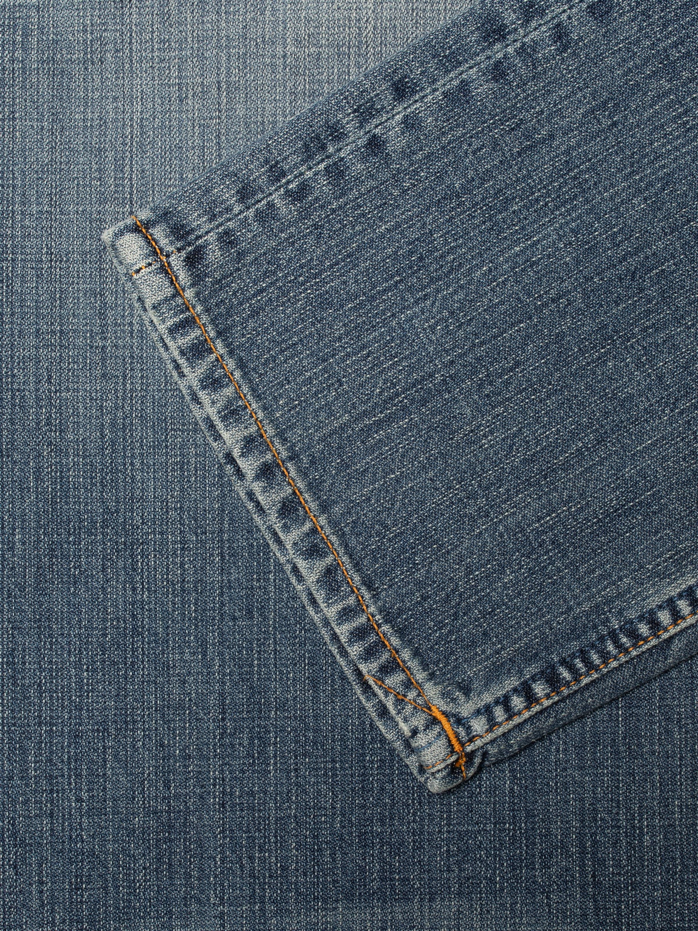 Nudie Jeans Rad Rufus Echoed Gold, close-up of the hem on mid blue wash organic cotton denim with orange stitching.