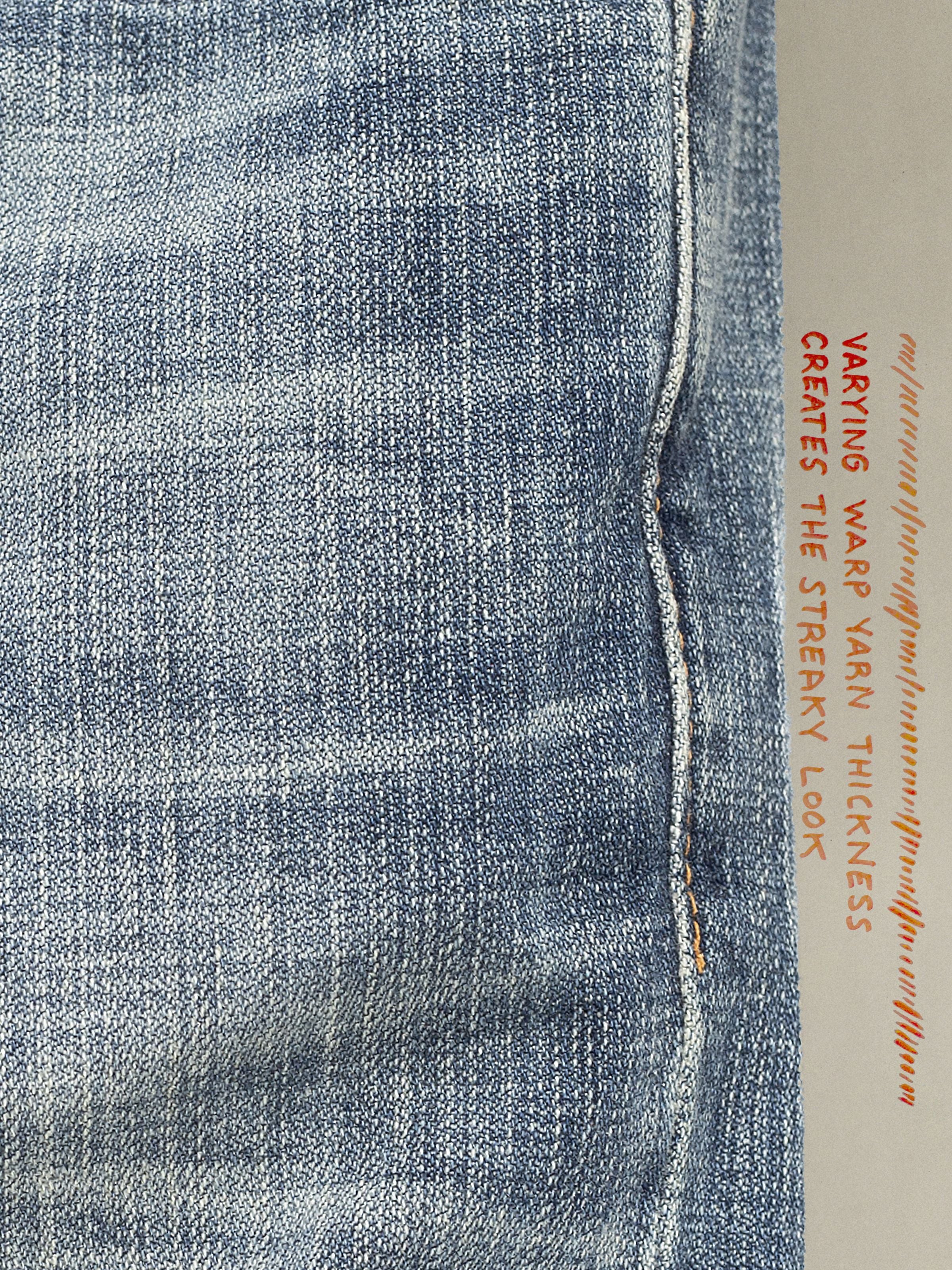 Nudie Jeans Gritty Jackson Tidal Waves, Nahaufnahme des streifigen Broken Twill Denim-Stoffs aus Bio-Baumwolle in Mid Blue.