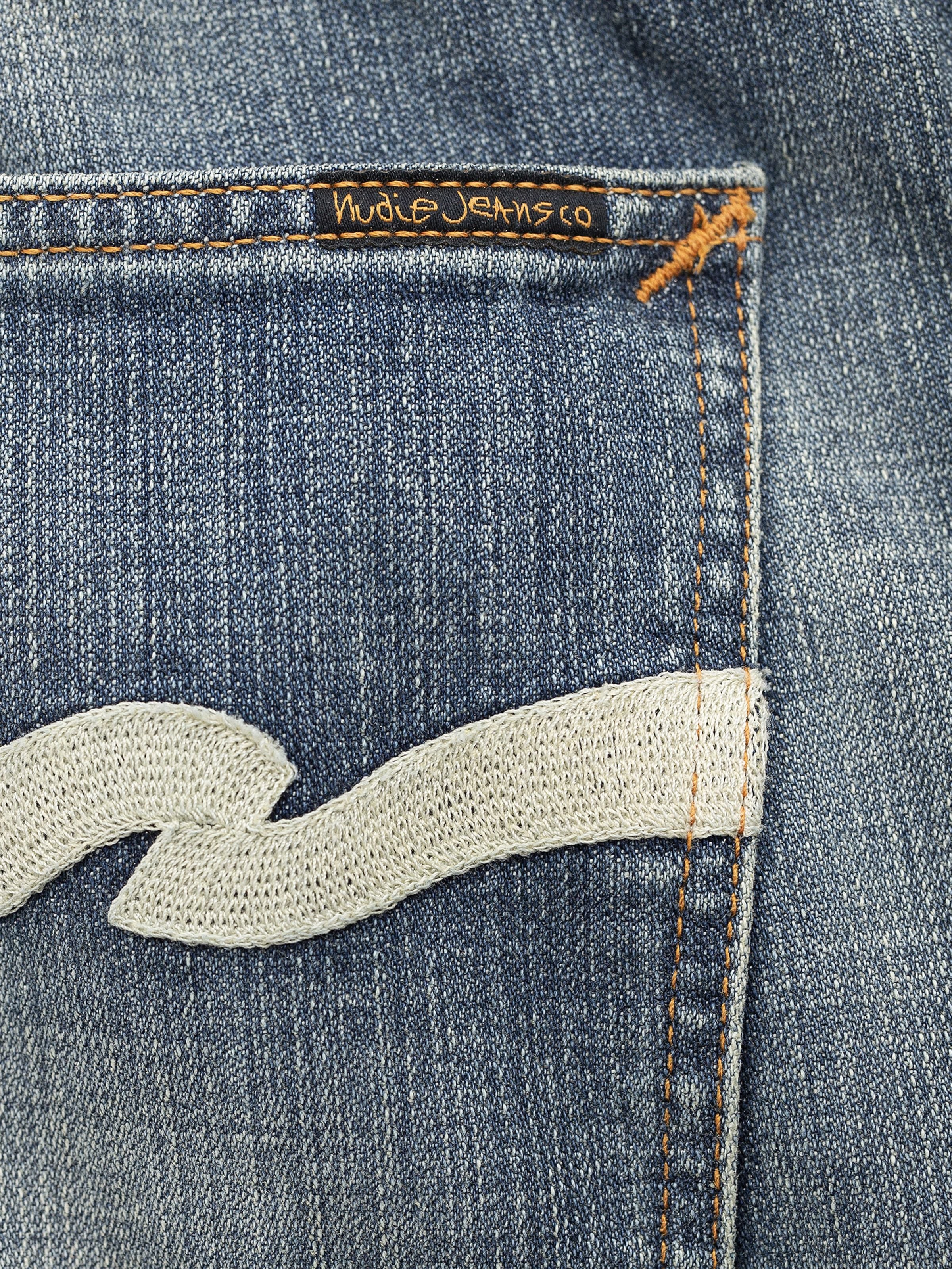 Nudie Jeans Gritty Jackson Tidal Waves, Nahaufnahme: ecrufarbene Gesäßtaschen-Stickerei auf mittelblauem Bio-Baumwoll-Denim.