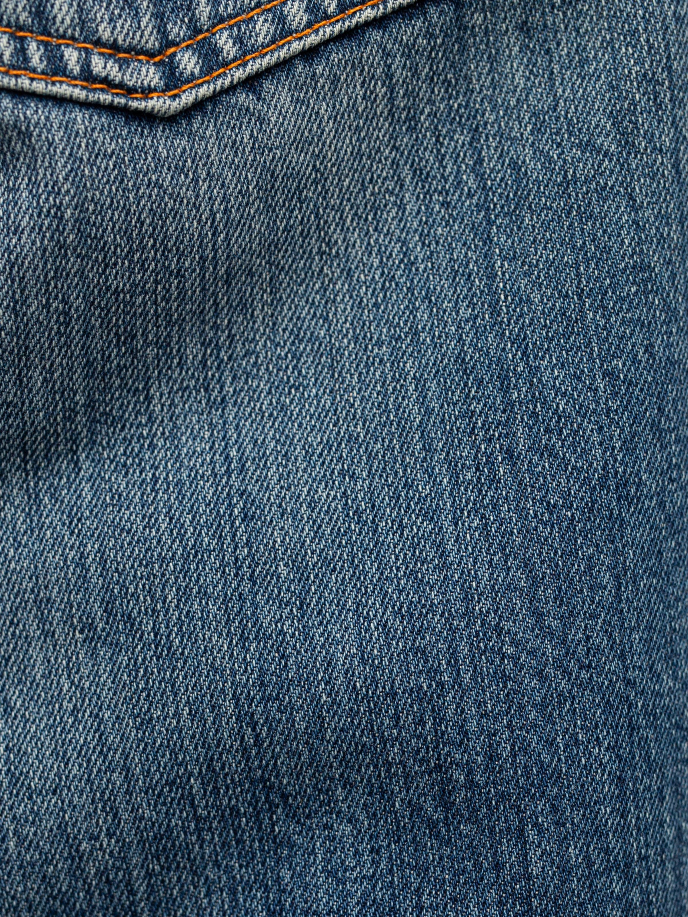 Nudie Jeans Tuff Tony Quiet Gold, a close-up of the mid blue organic cotton rigid denim fabric with vertical streaks.