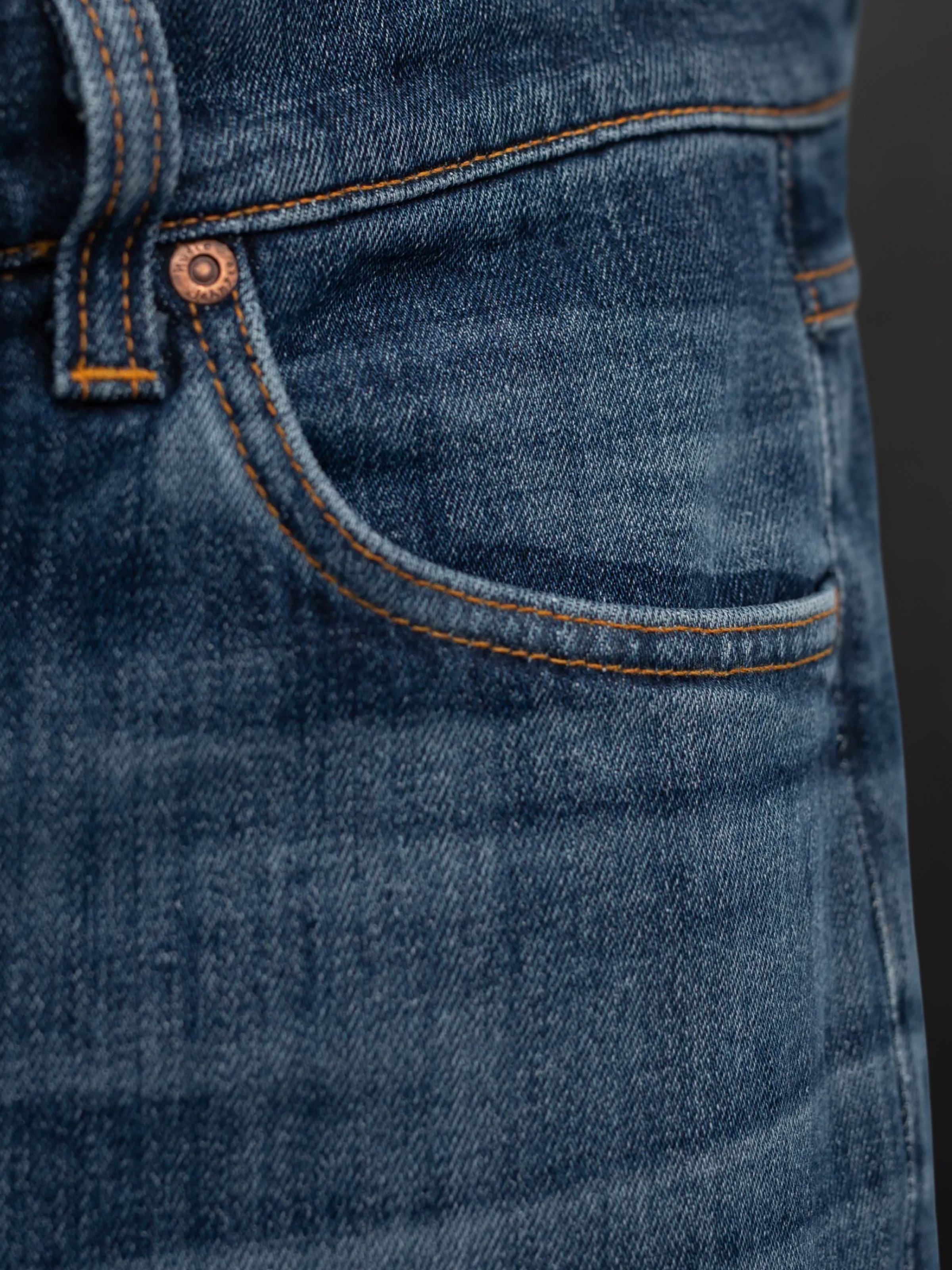 Nudie Jeans Lean Dean Echo Tracks, a close-up of the front pocket and copper rivet on washed blue organic cotton denim.