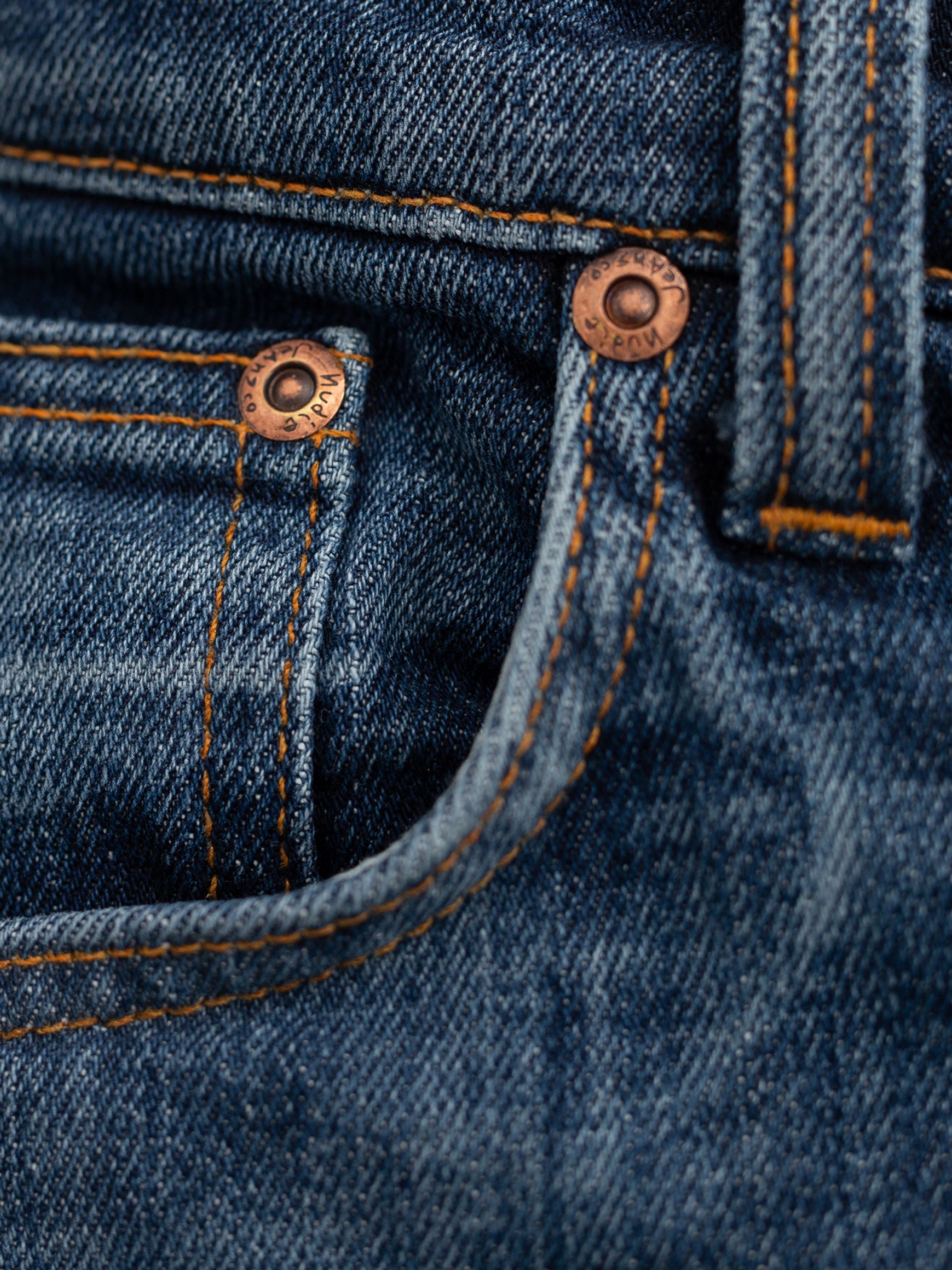 Nudie Jeans Lean Dean Echo Tracks, a close-up of the organic cotton denim with orange stitching and copper rivets.