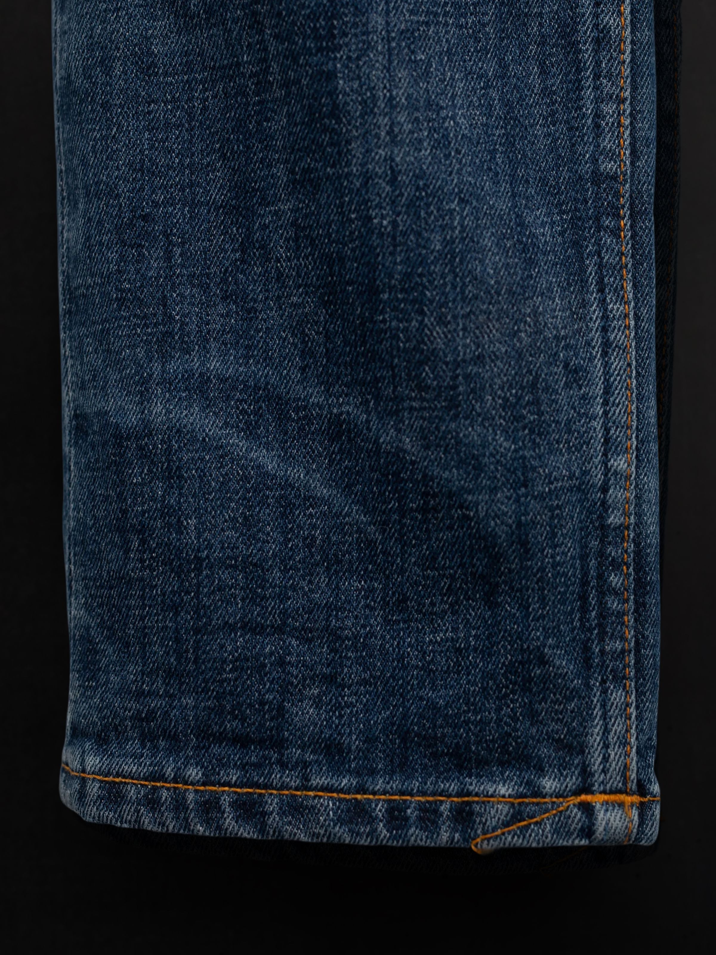 Nudie Jeans Lean Dean Echo Tracks, a close-up of the washed blue organic cotton denim with orange topstitching.