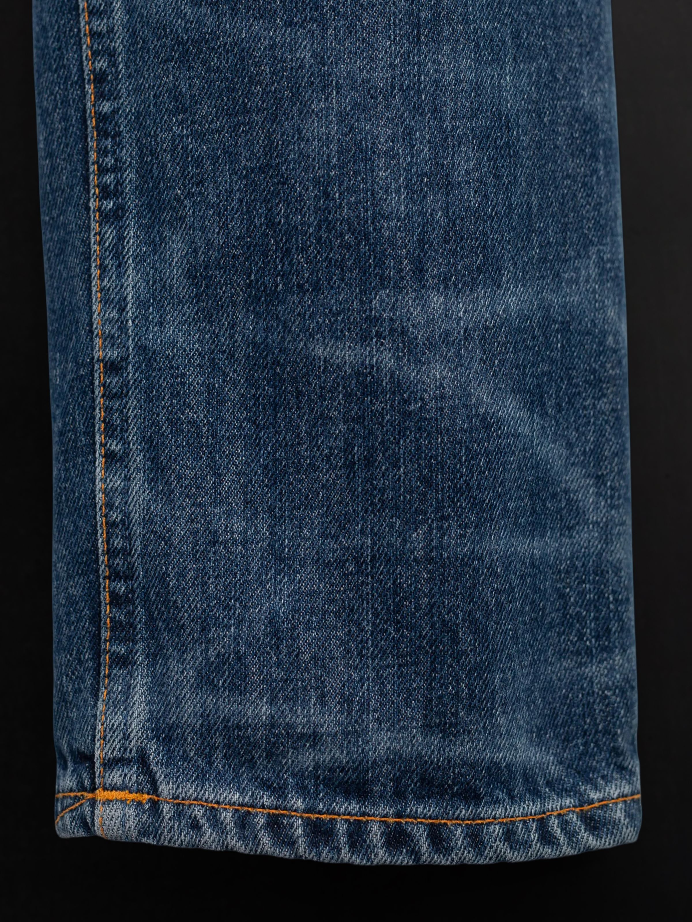 Nudie Jeans Steady Eddie II Twisted Tracks, Nahaufnahme von blauem Rigid Denim aus Bio-Baumwolle mit orangefarbenen Nähten.