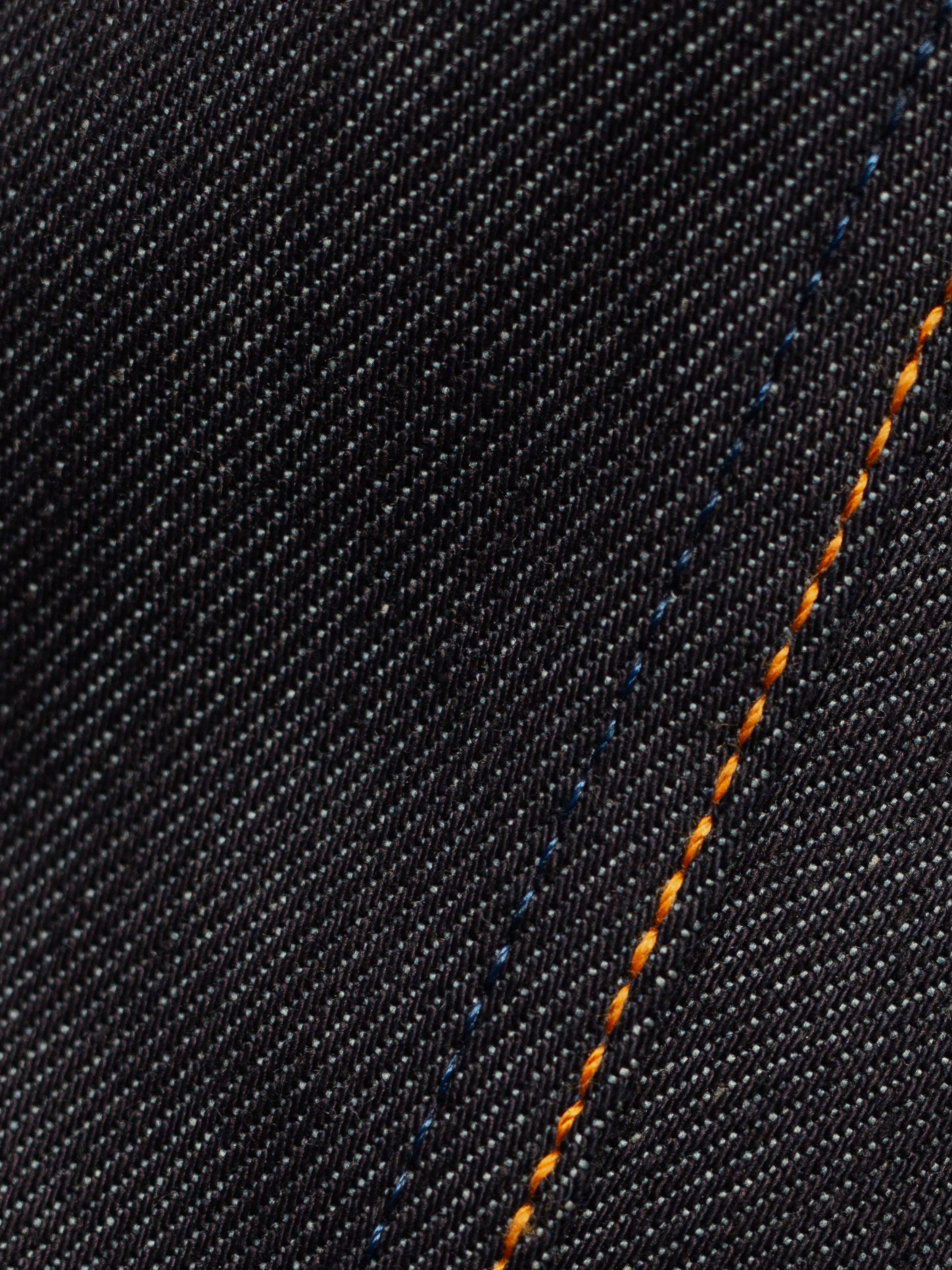 Nudie Jeans Loud Larry Lightning Selvage, Nahaufnahme der Selvedge-Denim-Textur mit orangen Nähten.
