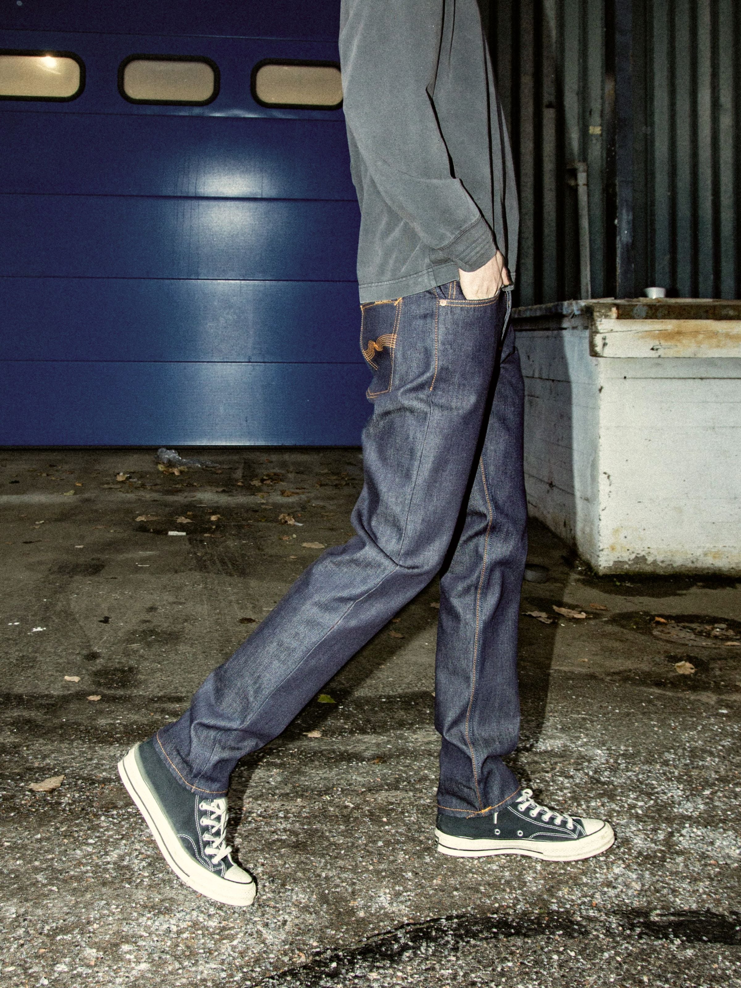 Nudie Jeans Steady Eddie II Dry One, Tapered-Jeans aus Rigid Bio-Baumwoll-Denim in Indigo, von einem gehenden Model getragen.