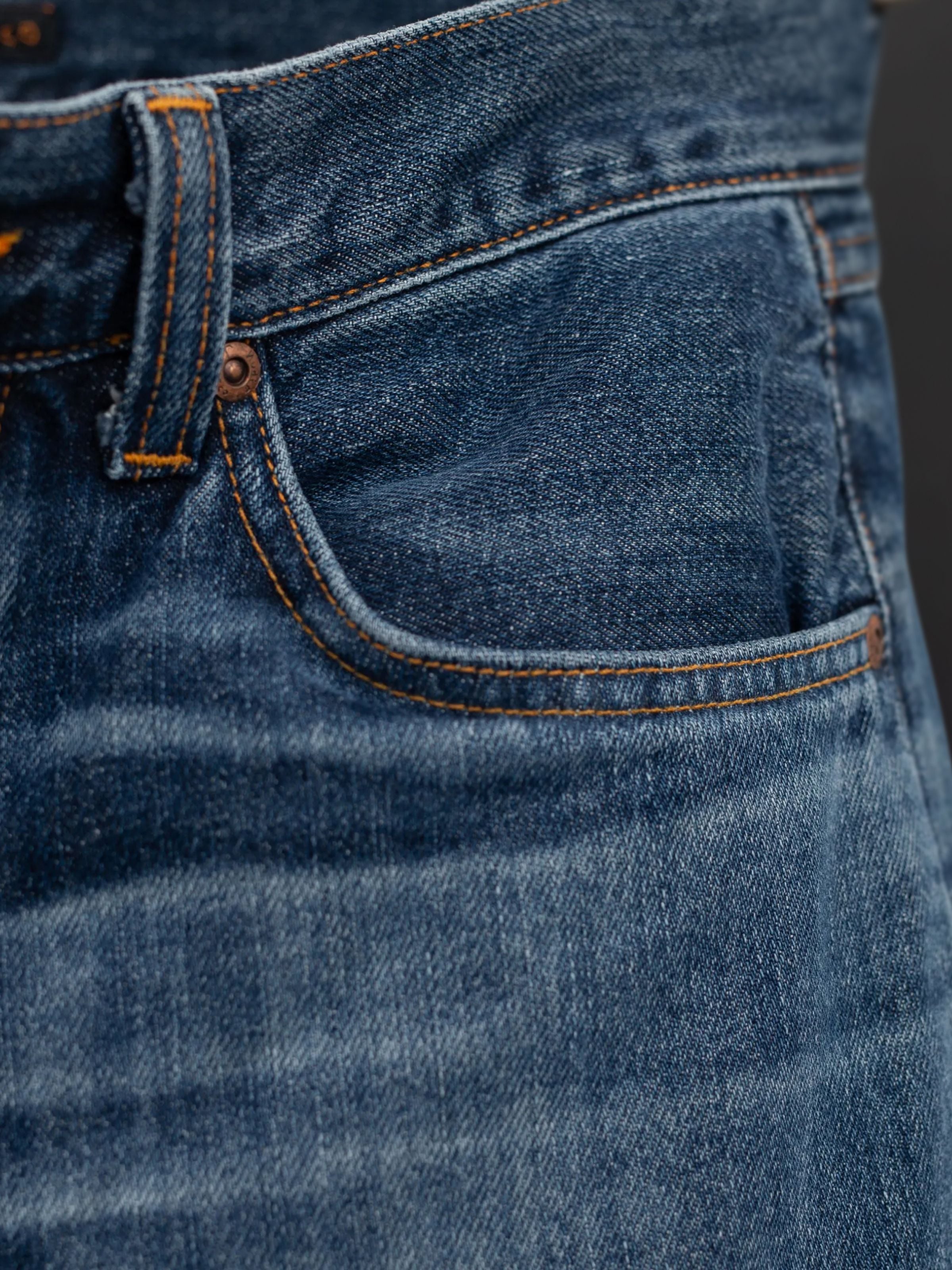 Nudie Jeans Rad Rufus Blue Twisted Tracks, a close-up of the front pocket area in indigo organic cotton rigid denim.