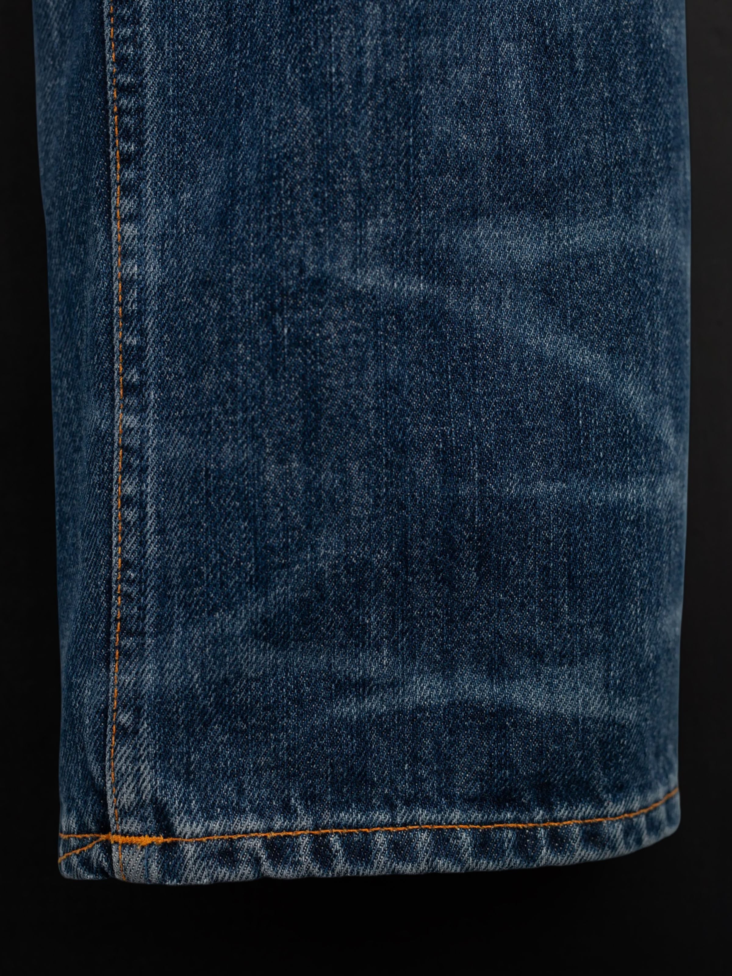 Nudie Jeans Rad Rufus Blue Twisted Tracks, a close-up of the washed indigo organic cotton denim with orange stitching.