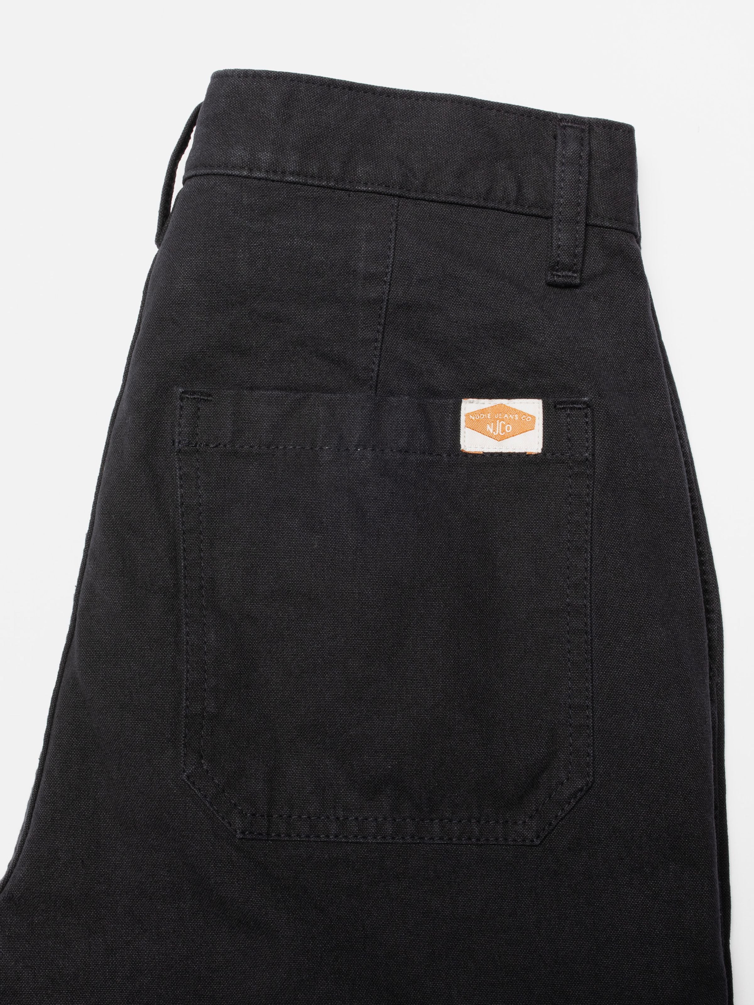 Nudie Jeans Wendy Pants aus schwarzer Bio-Baumwolle Duck Canvas, Nahaufnahme der Gesäßtasche mit gewebtem Logo-Patch.
