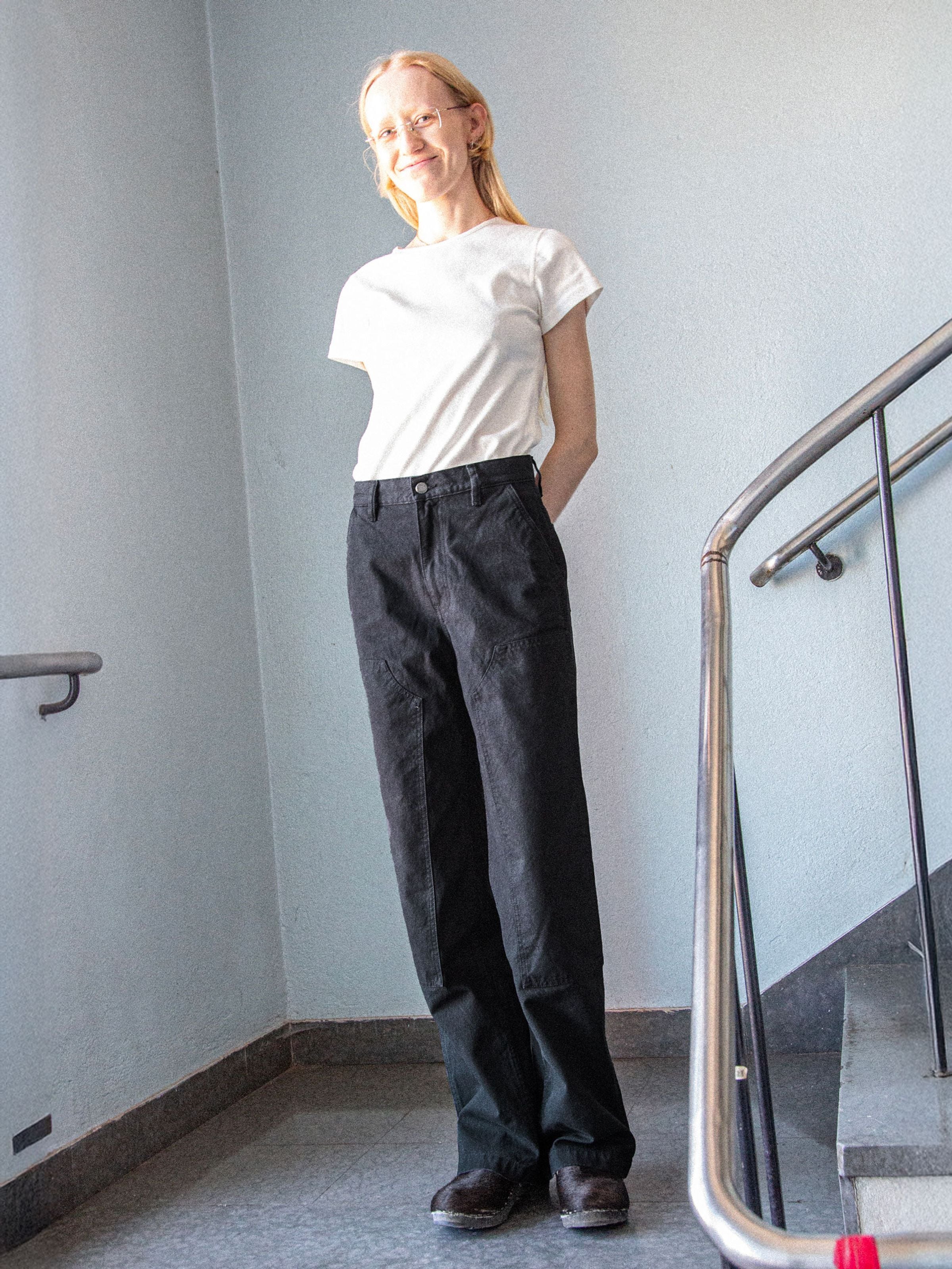 Nudie Jeans Wendy Pants in Black, Wide-Leg-Hose aus Duck Canvas aus Bio-Baumwolle, von einem Model im Treppenhaus getragen.