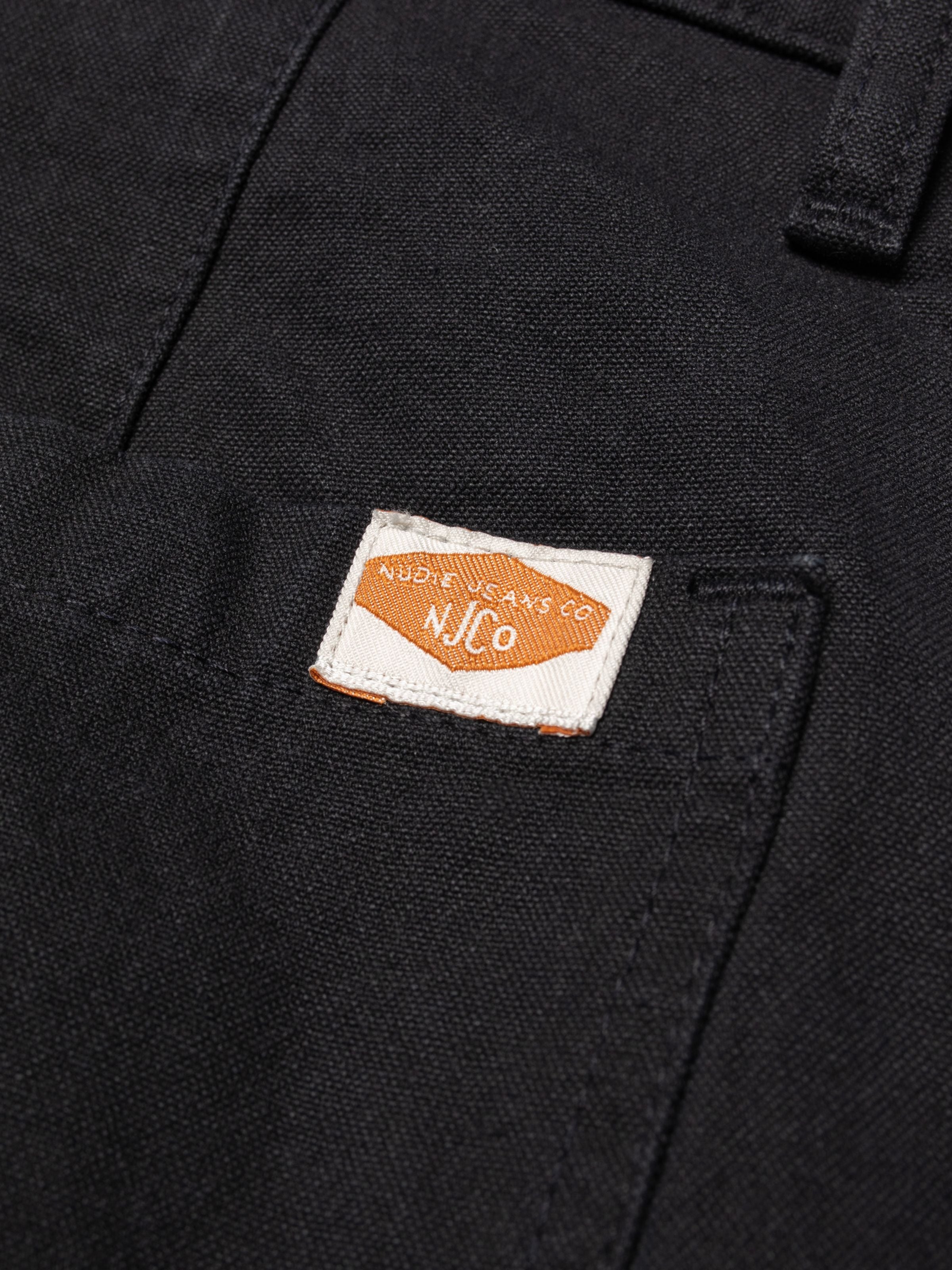 Nudie Jeans Wendy Pants Duck Canvas in Schwarz, Nahaufnahme des gewebten Marken-Patches auf Canvas aus Bio-Baumwolle.