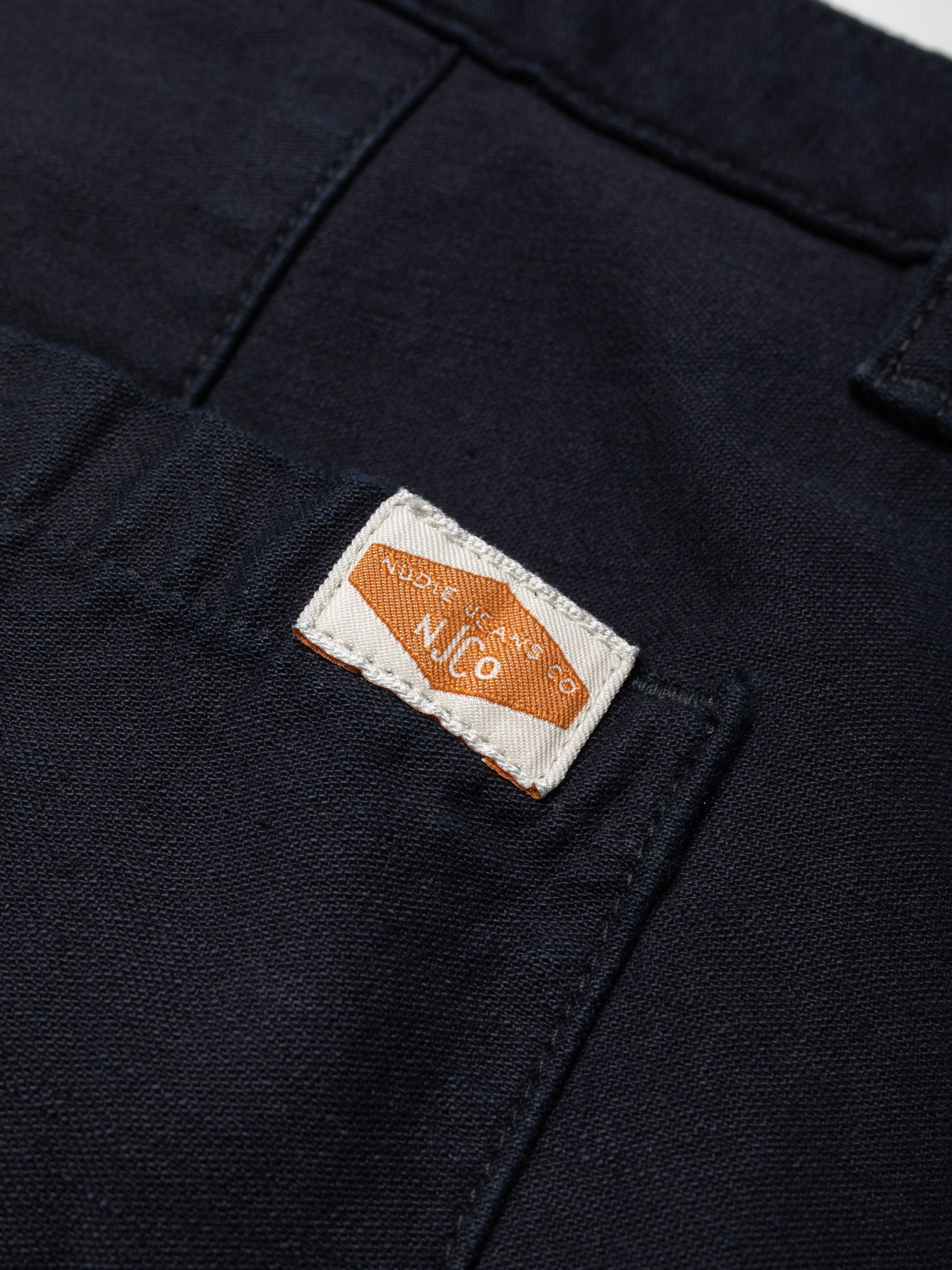 Nudie Jeans Wendy Pants Back Sateen Indigo, Nahaufnahme des gewebten Marken-Patches auf der tiefblauen Bio-Baumwolle.