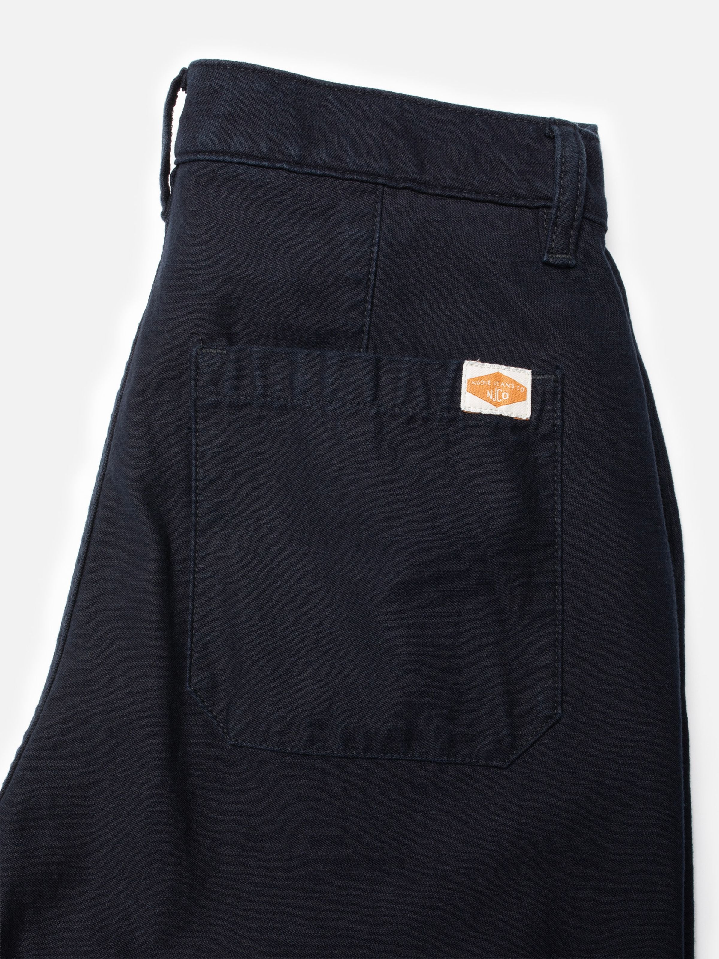 Nudie Jeans Wendy Pants Back Sateen Indigo, Nahaufnahme der Gesäßtasche mit gewebtem Logo-Patch auf Bio-Baumwolle.