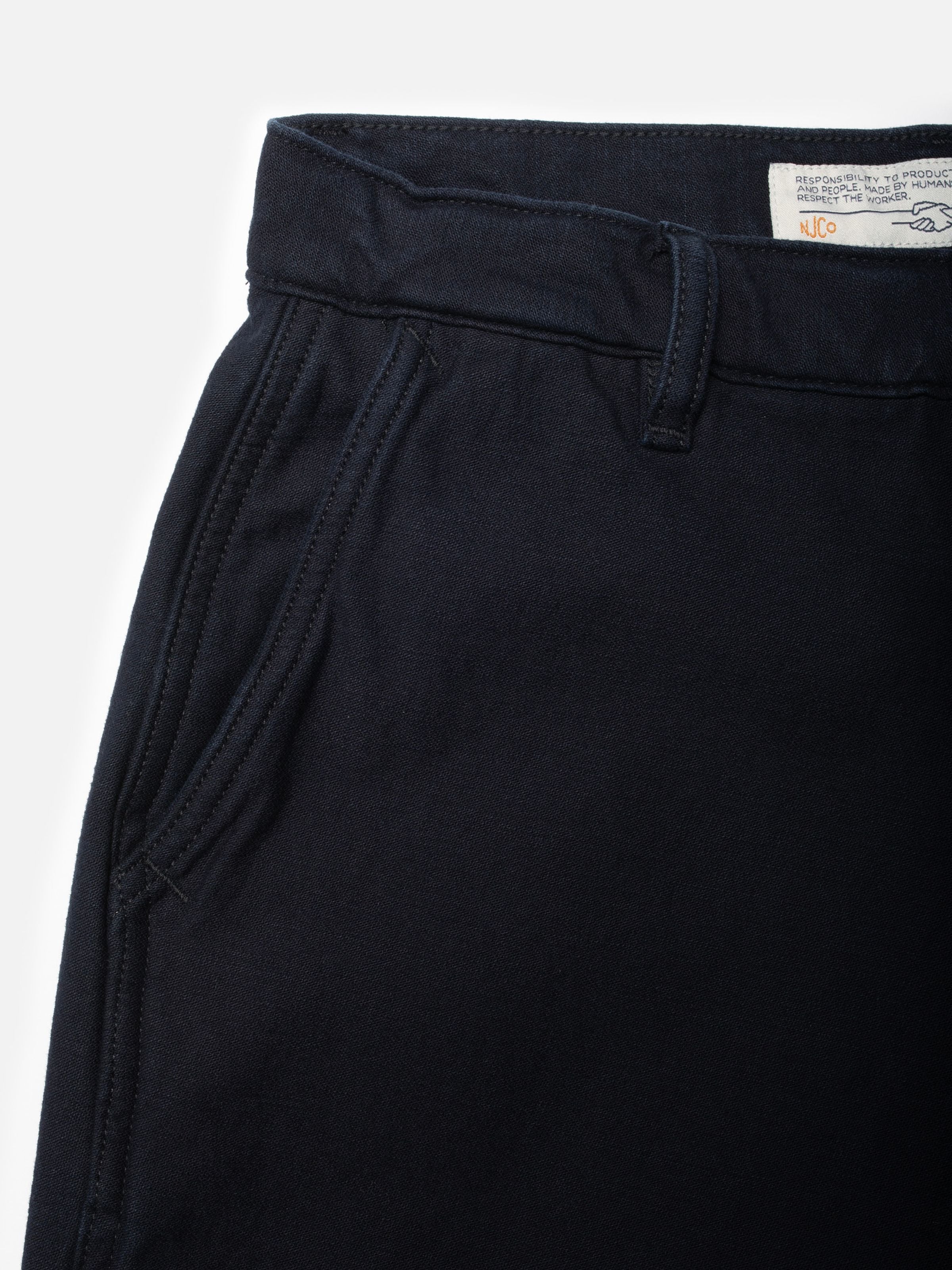 Nudie Jeans Wendy Pants Back Sateen Indigo, Nahaufnahme des Stoffs aus Bio-Baumwolle, Vordertasche und Hosenbund.