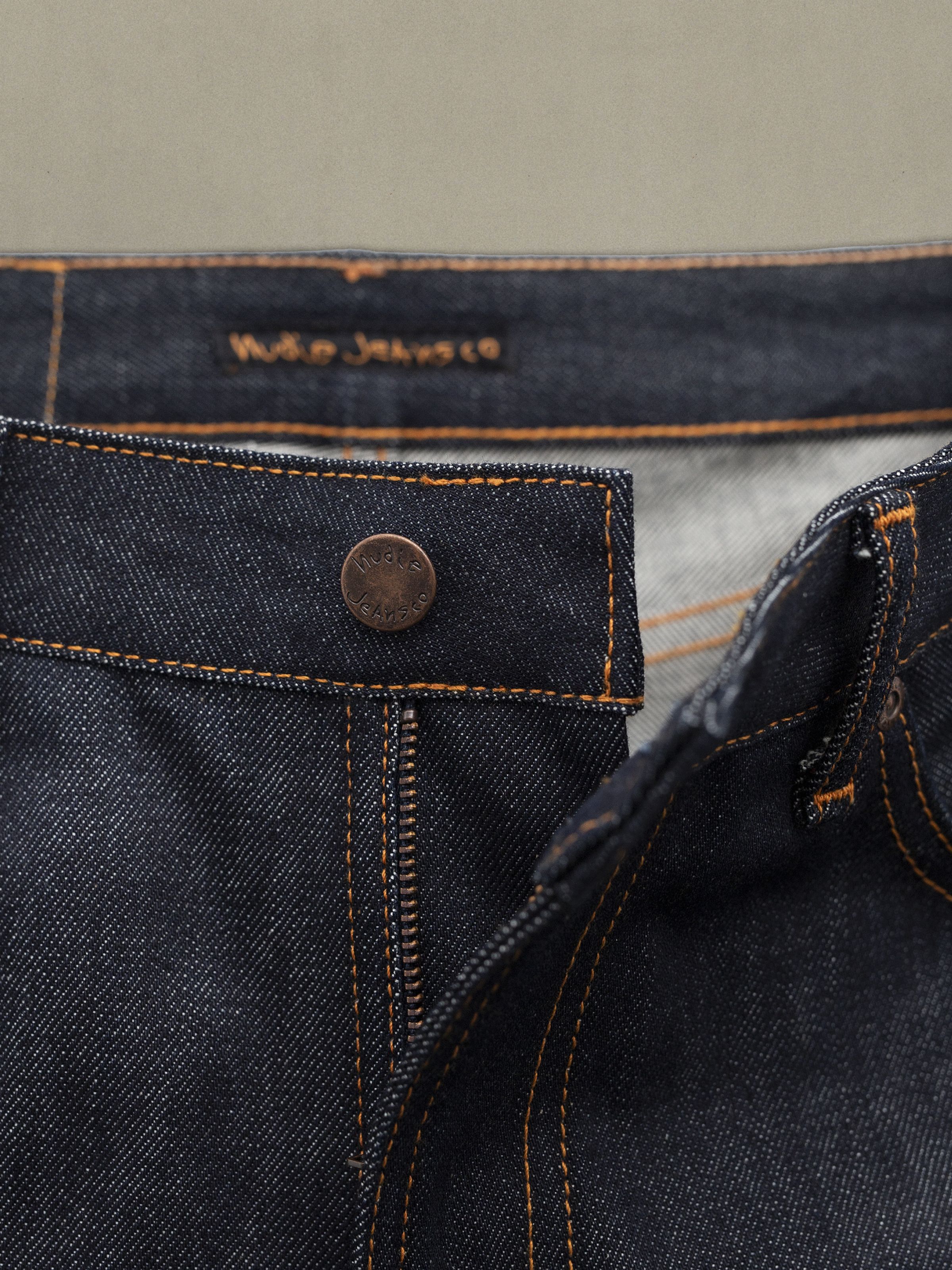 Nudie Jeans Sonic Sue Dry Ecru Waves, a close-up of the copper button and orange stitching on rigid organic cotton denim.