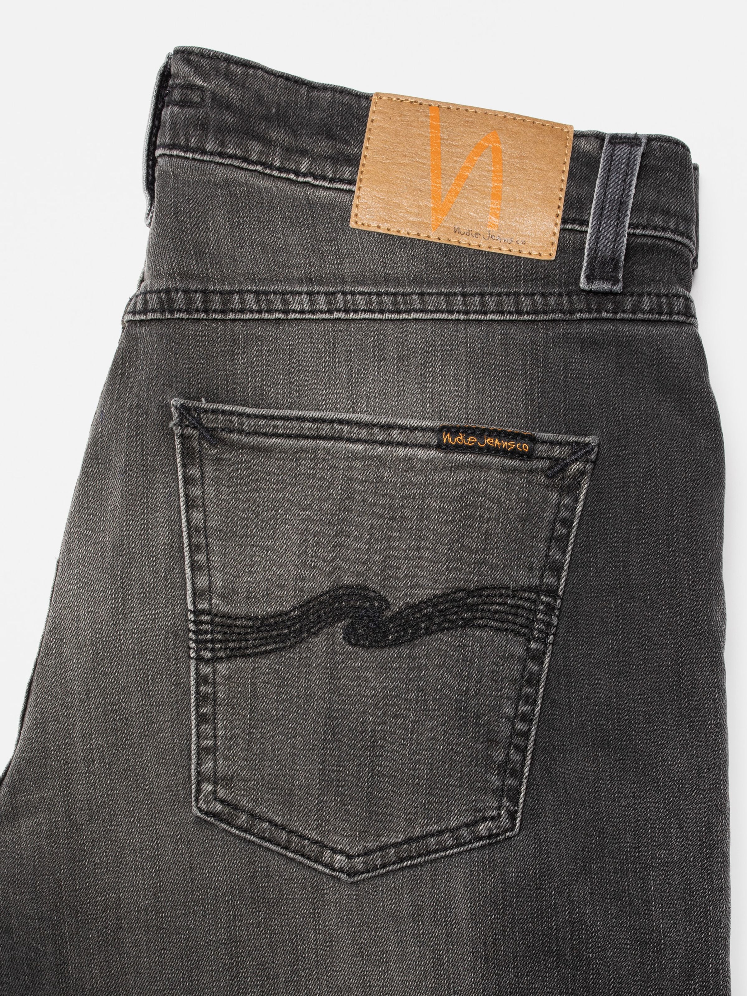 Nudie Jeans Solid Ollie Black Mist, close-up of back pocket and Jacron patch on mid-grey organic cotton stretch denim.
