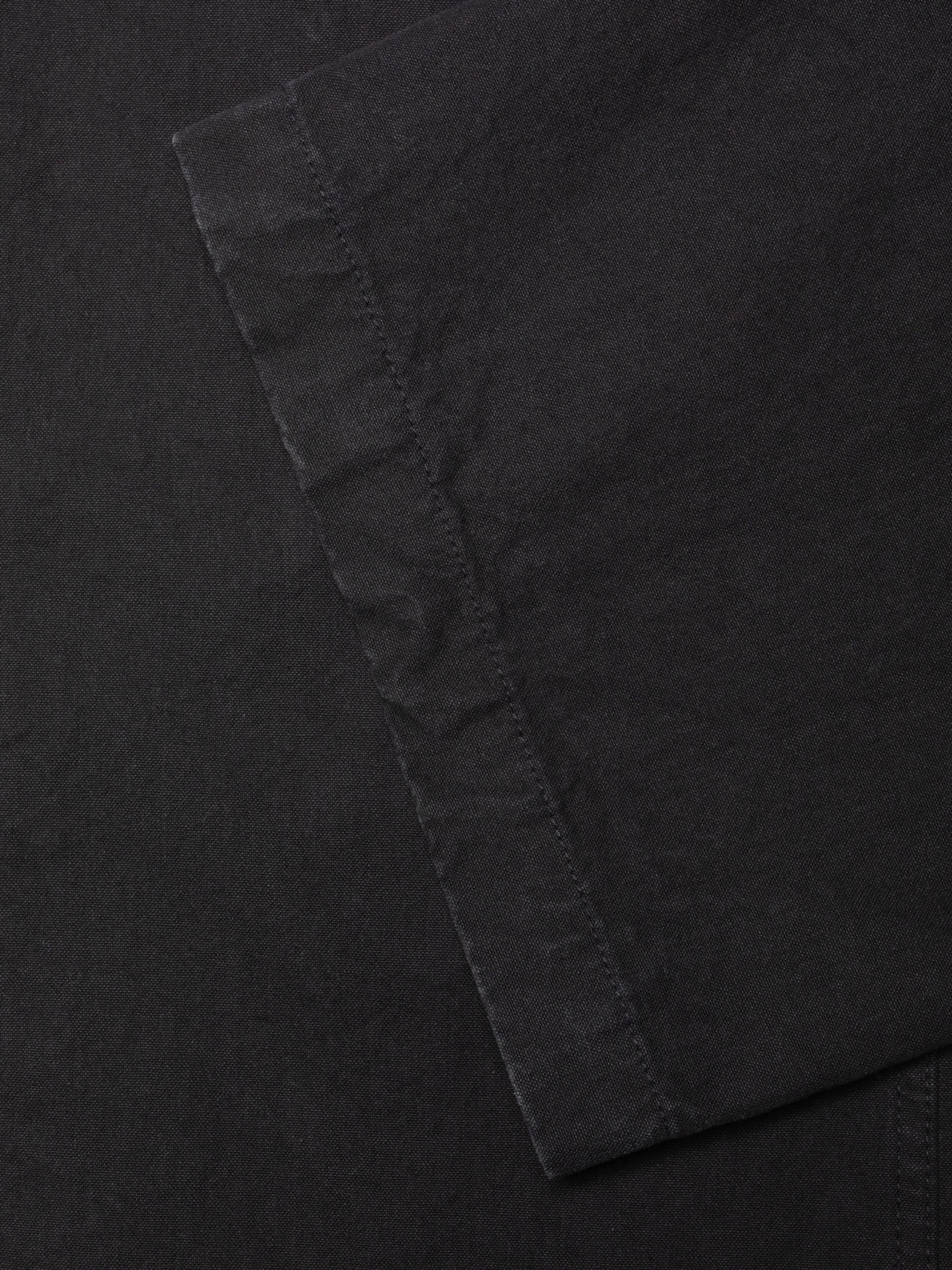 Nudie Jeans Klara Dungarees Duck Canvas, a close-up of the pitch-black textured duck canvas fabric and stitched seam.