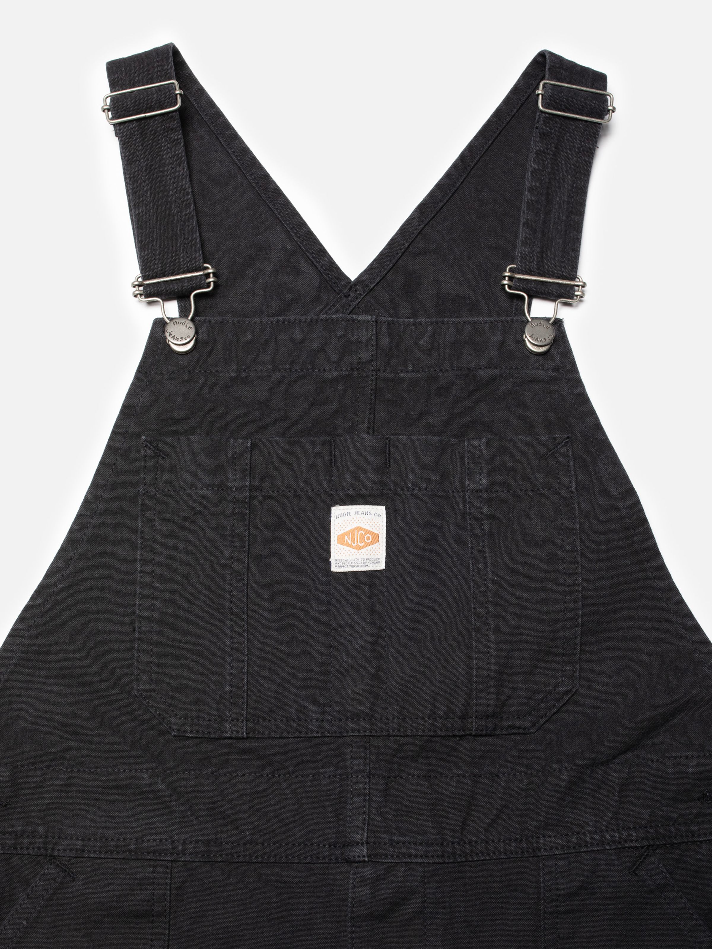 Nudie Jeans Klara Dungarees Duck Canvas, close-up of the front bib pocket and straps in black organic cotton duck canvas.