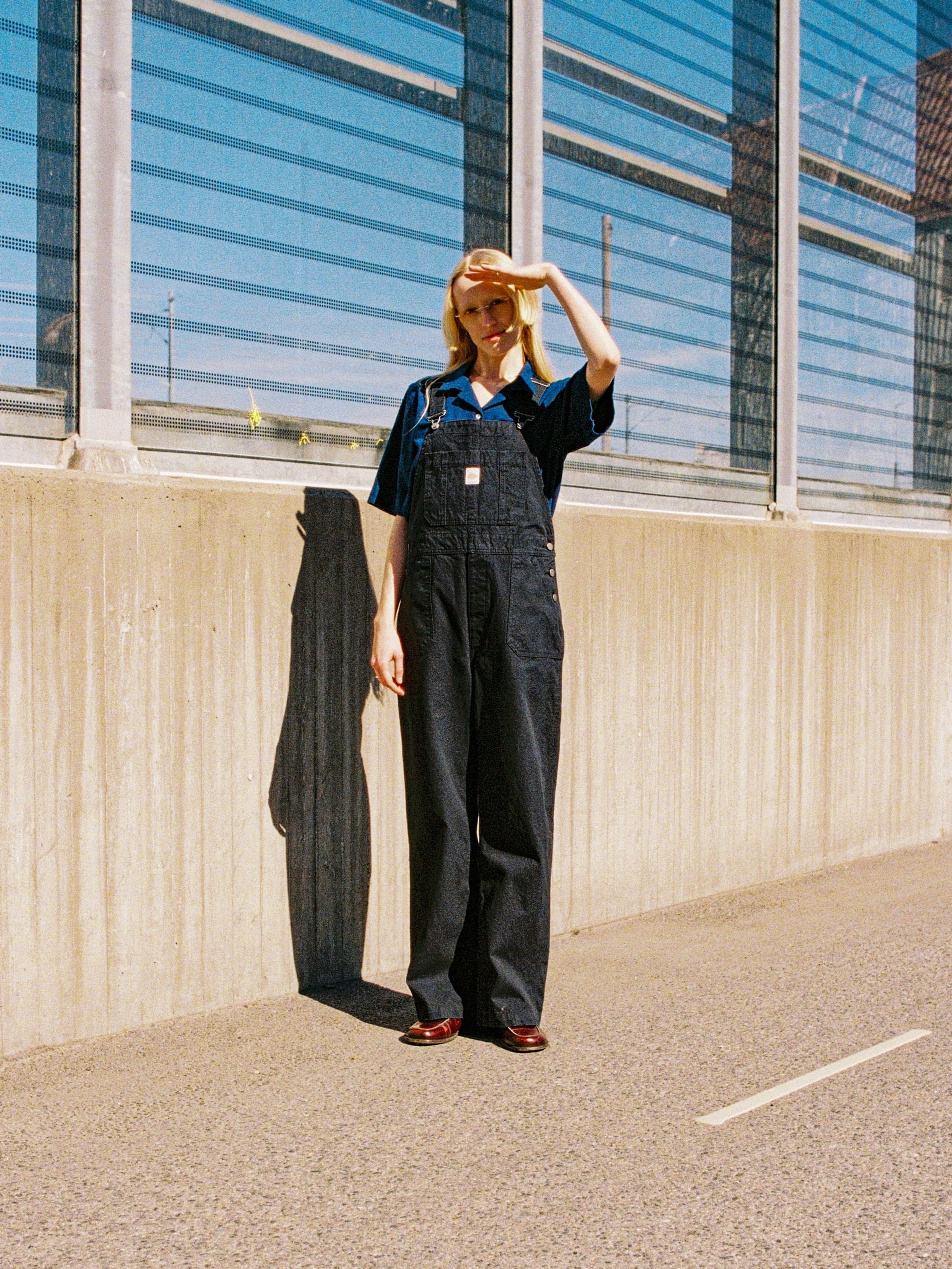 Nudie Jeans Klara Dungarees Duck Canvas, a model wearing regular fit black duck canvas dungarees outdoors.