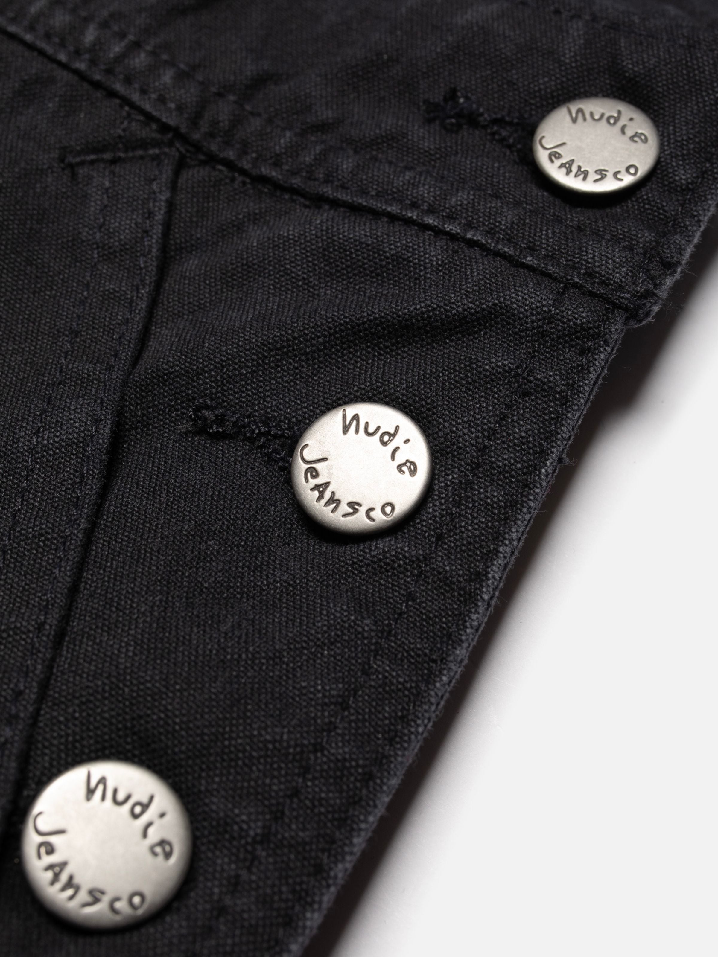 Nudie Jeans Klara Dungarees Duck Canvas, close-up of the black organic cotton duck canvas fabric and metal buttons.