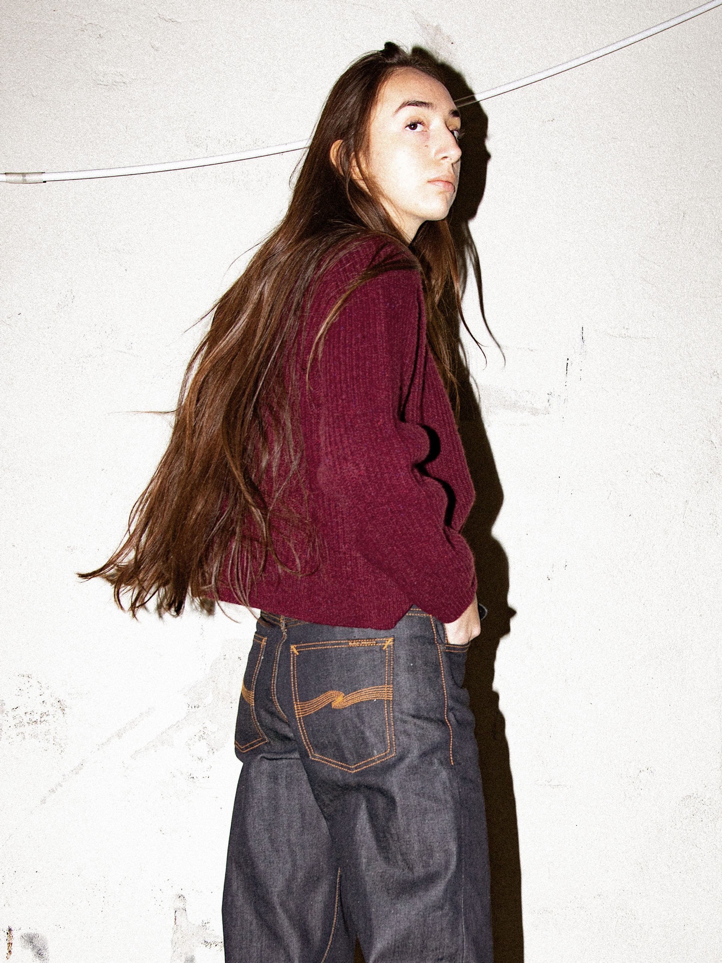 Nudie Jeans Ellen Cardigan Wool in Burgundy, Rundhals-Cardigan aus Bio-Wolle an einem Model in dunklem Denim.