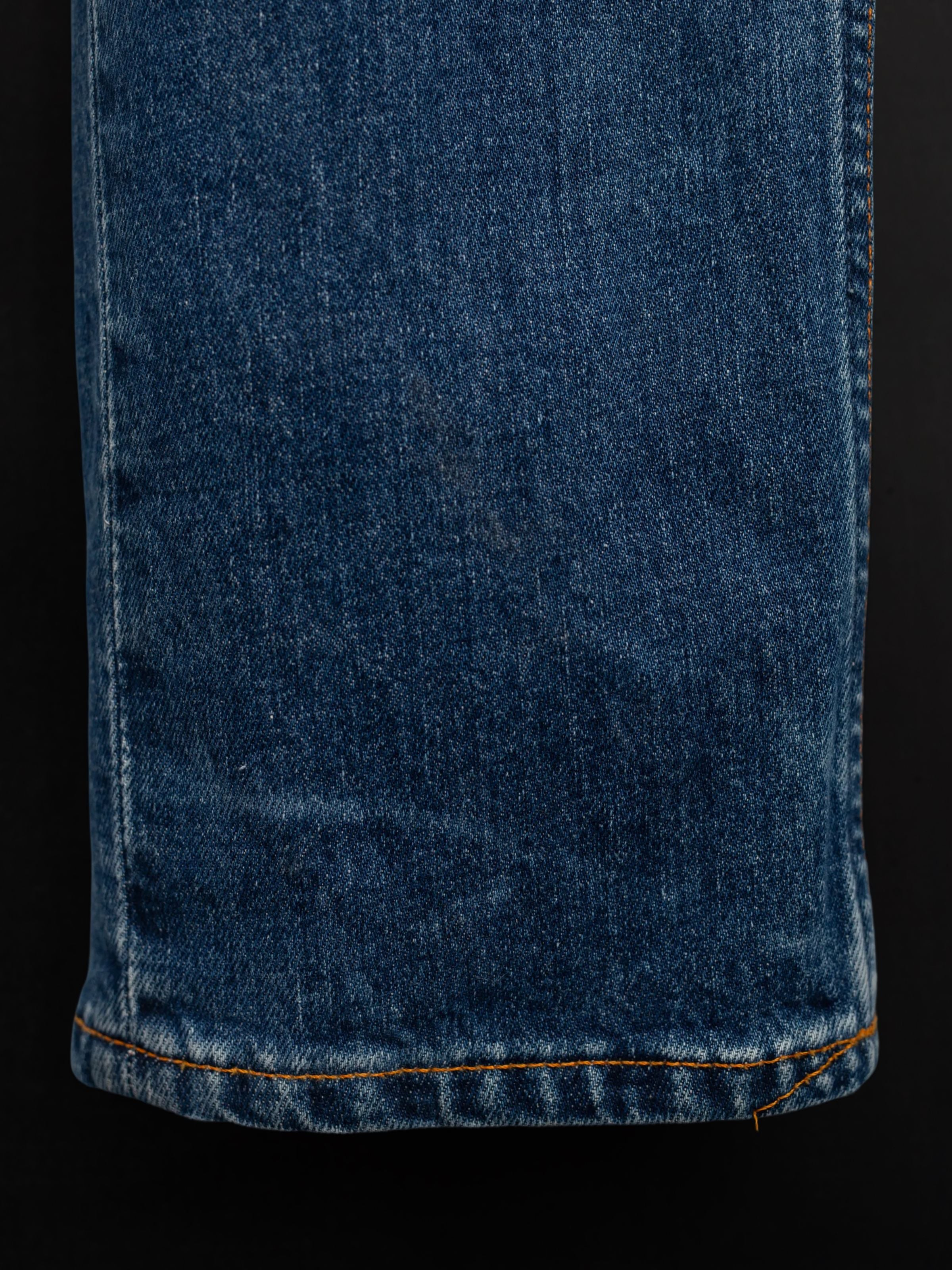 Nudie Jeans Grim Tim Life Tracks, close-up of the mid blue organic cotton stretch denim fabric and orange hem stitching.